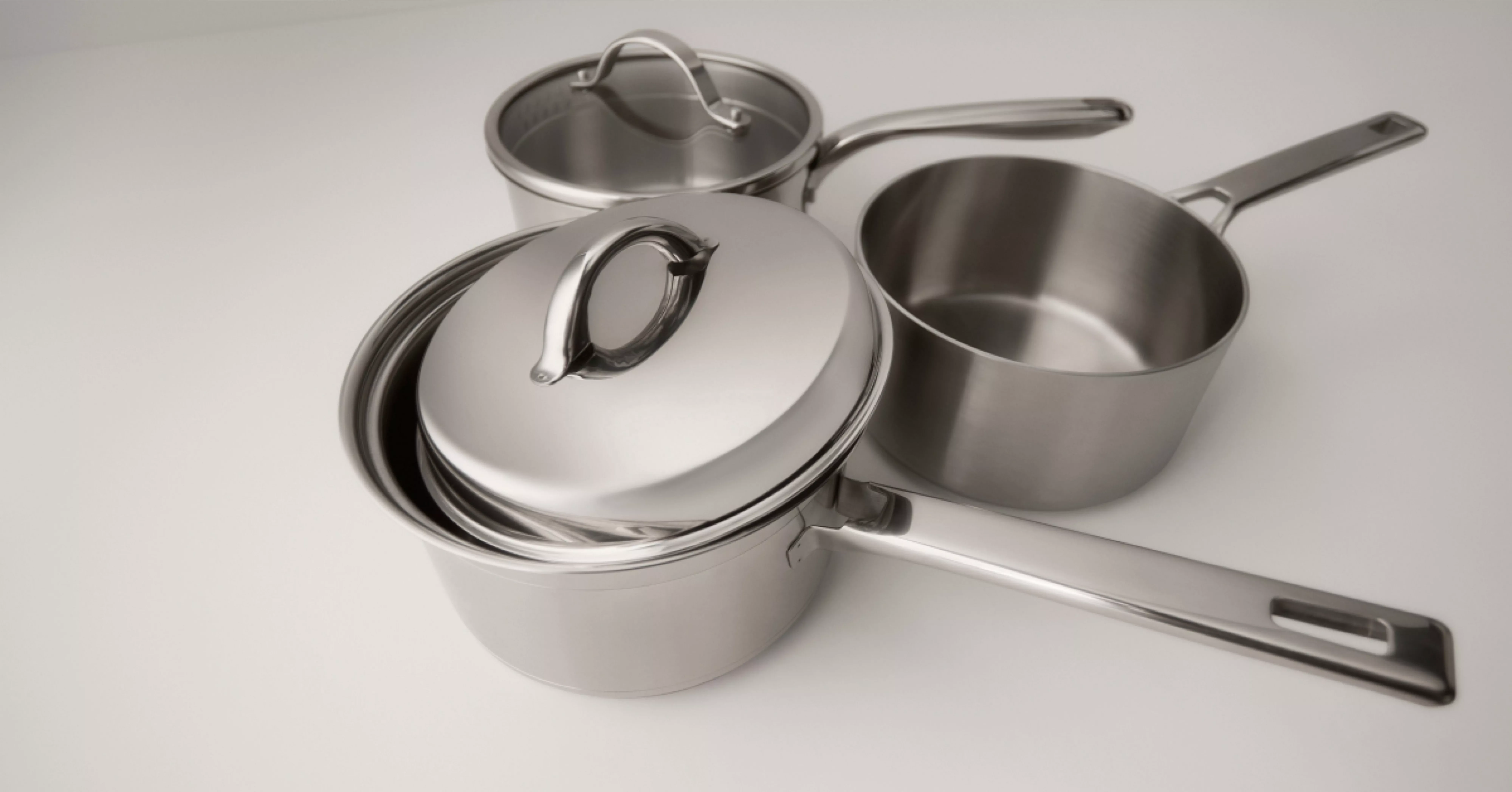 Stainless steel saucepan set with lids and long handles, modern cookware on a light kitchen worktop