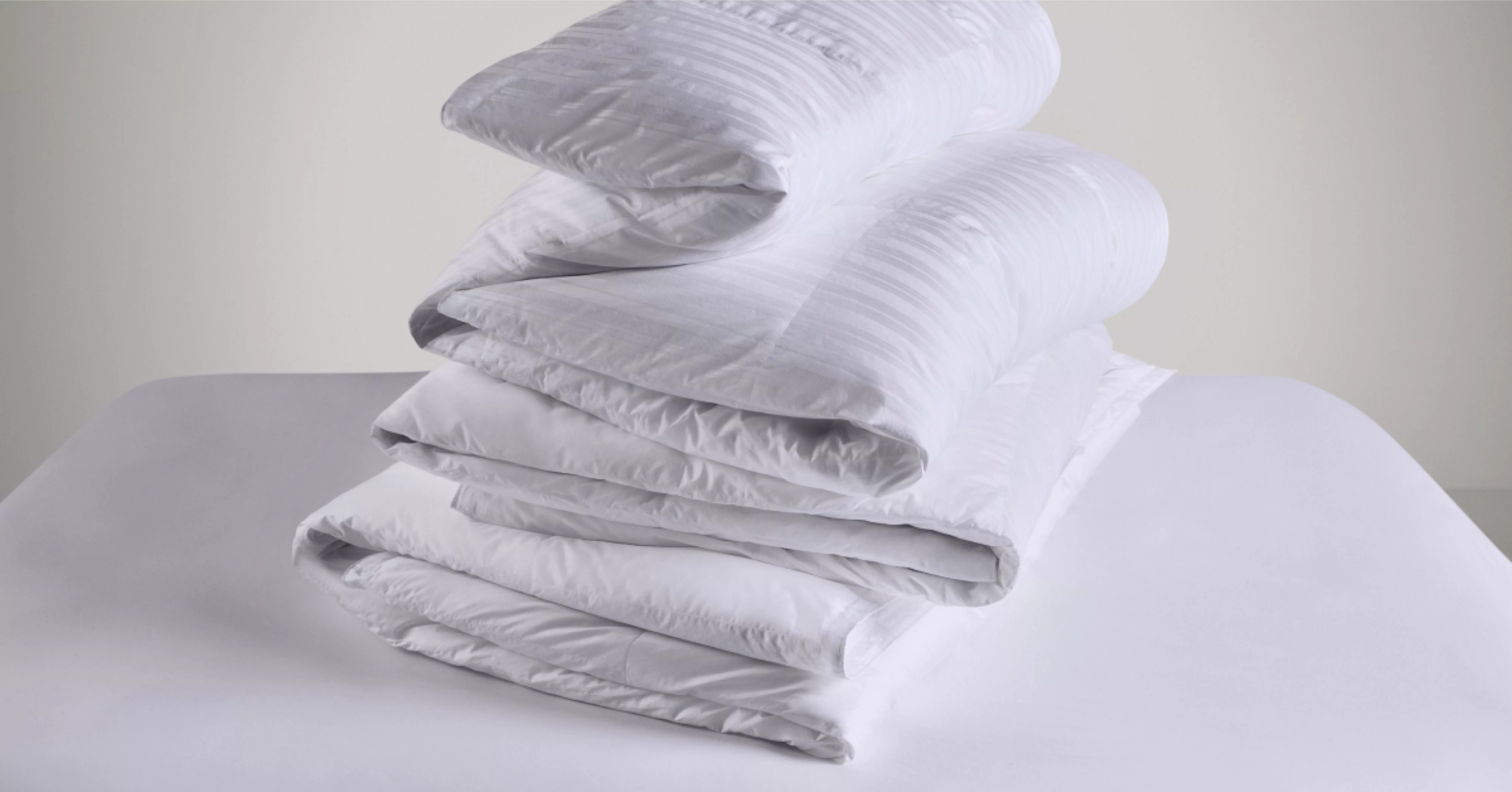 Stack of folded white duvet and bedding on a bed, clean minimalist bedroom linen for cosy sleep comfort