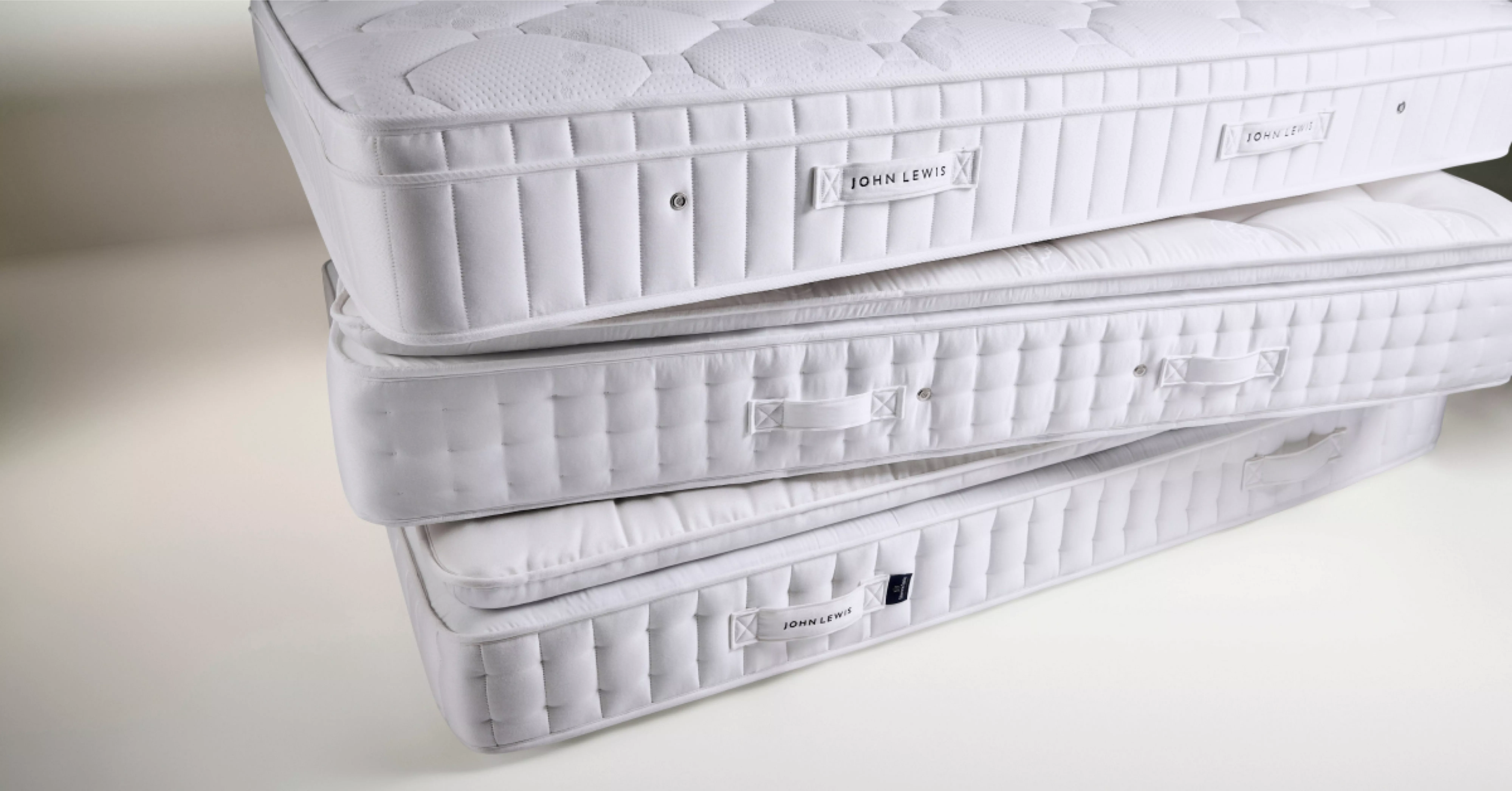 Stacked white John Lewis pocket sprung mattresses with quilted covers, showing side handles and branding labels