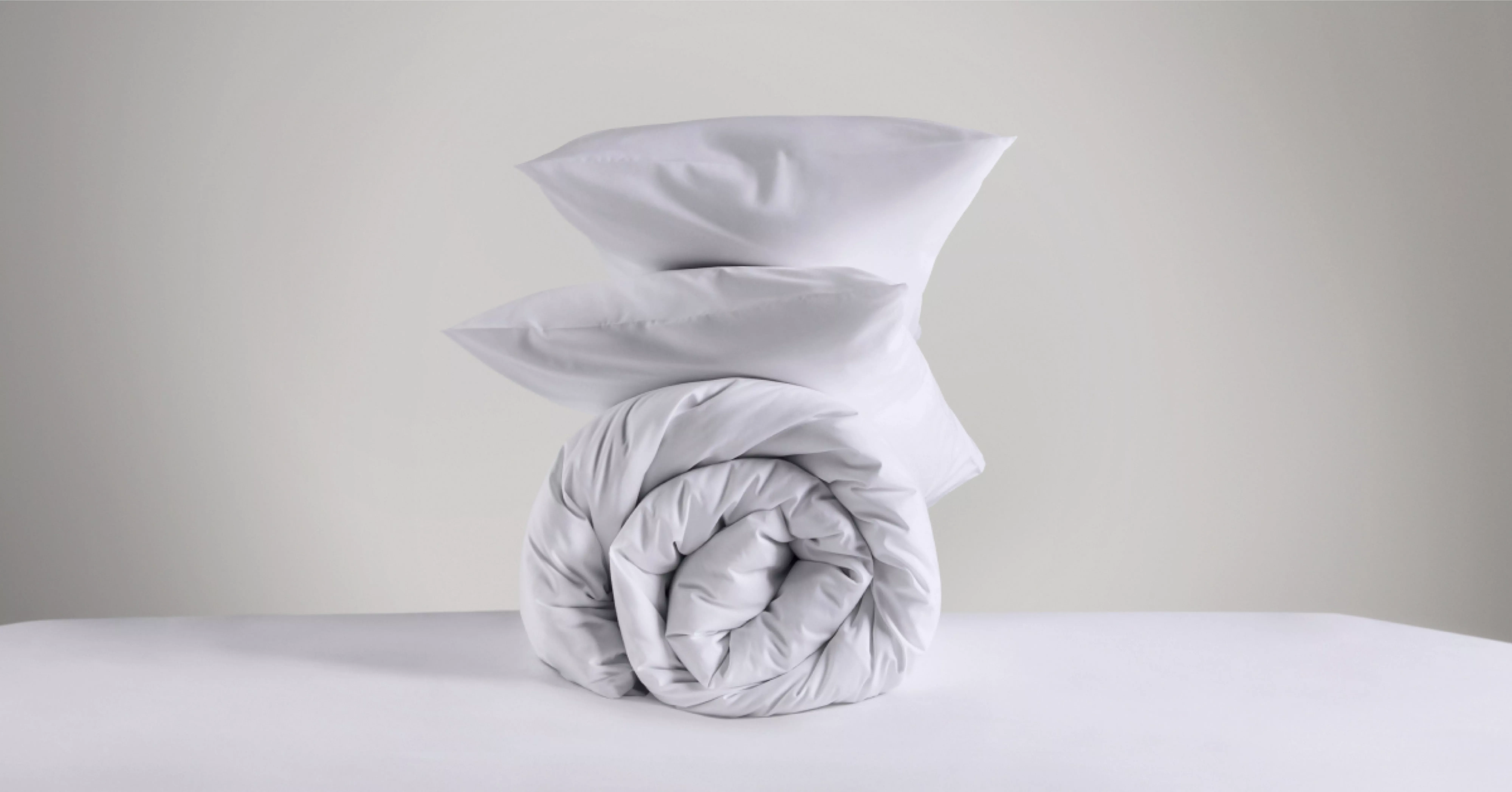 Stack of folded white duvet and pillows on a bed, soft hotel-style bedding set for a clean, cosy bedroom look