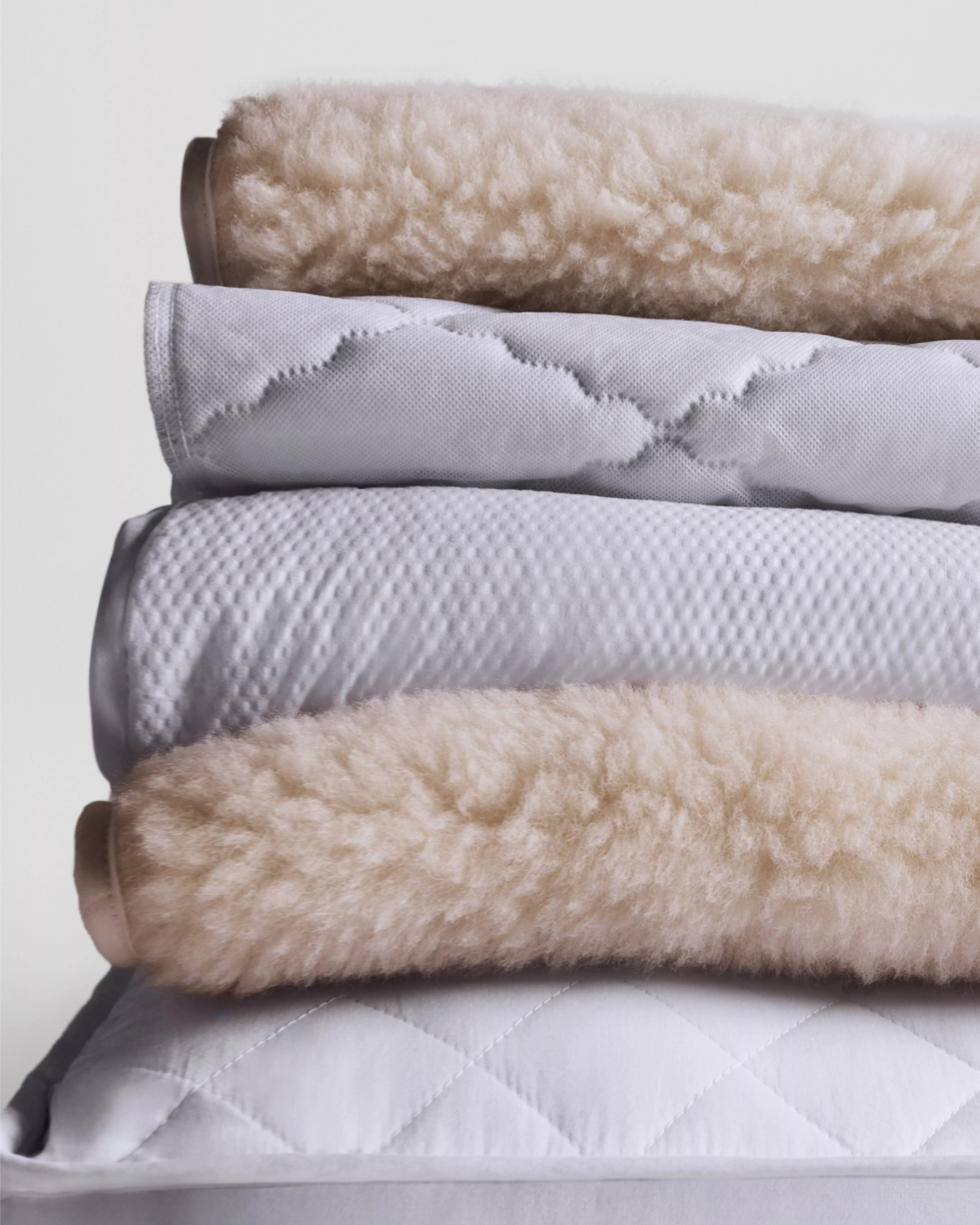 Stacked mattress toppers showing wool fleece and quilted covers, highlighting breathable bedding comfort layers