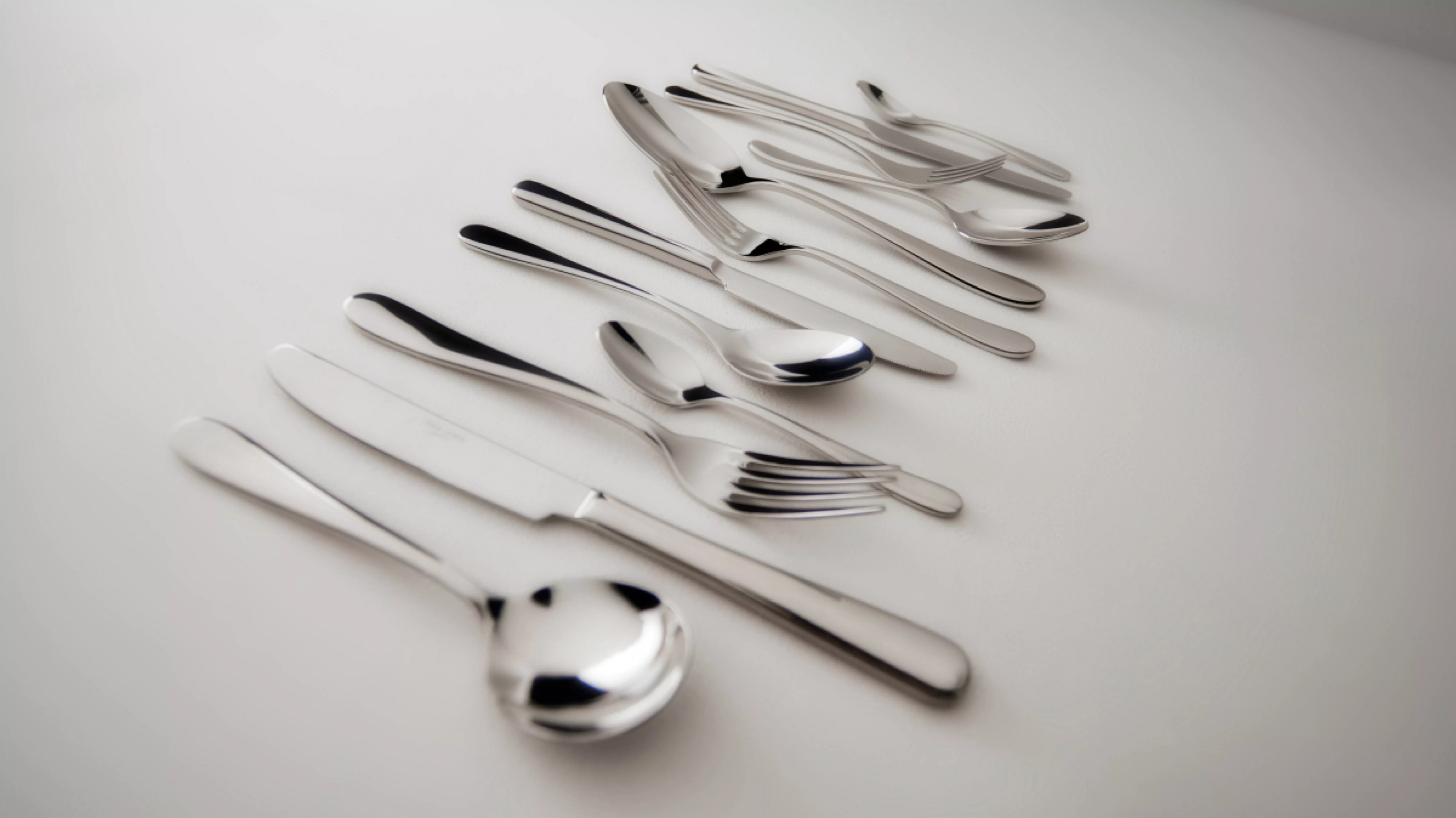 Stainless steel cutlery set with spoons, forks and knives neatly arranged on a white tabletop background