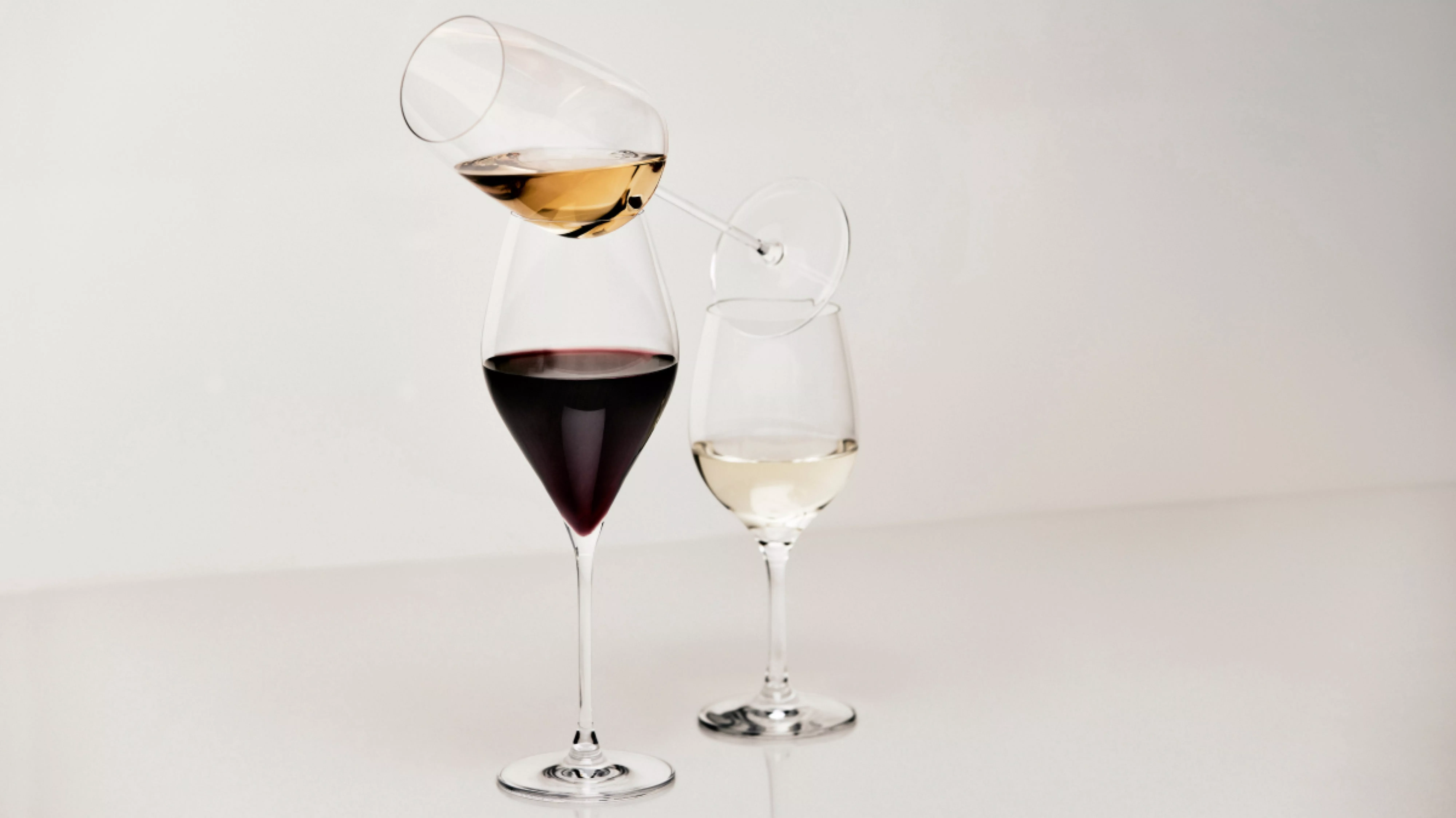 Minimalist studio photo of stacked wine glasses with red, white and rosé wine, balanced on a clear surface