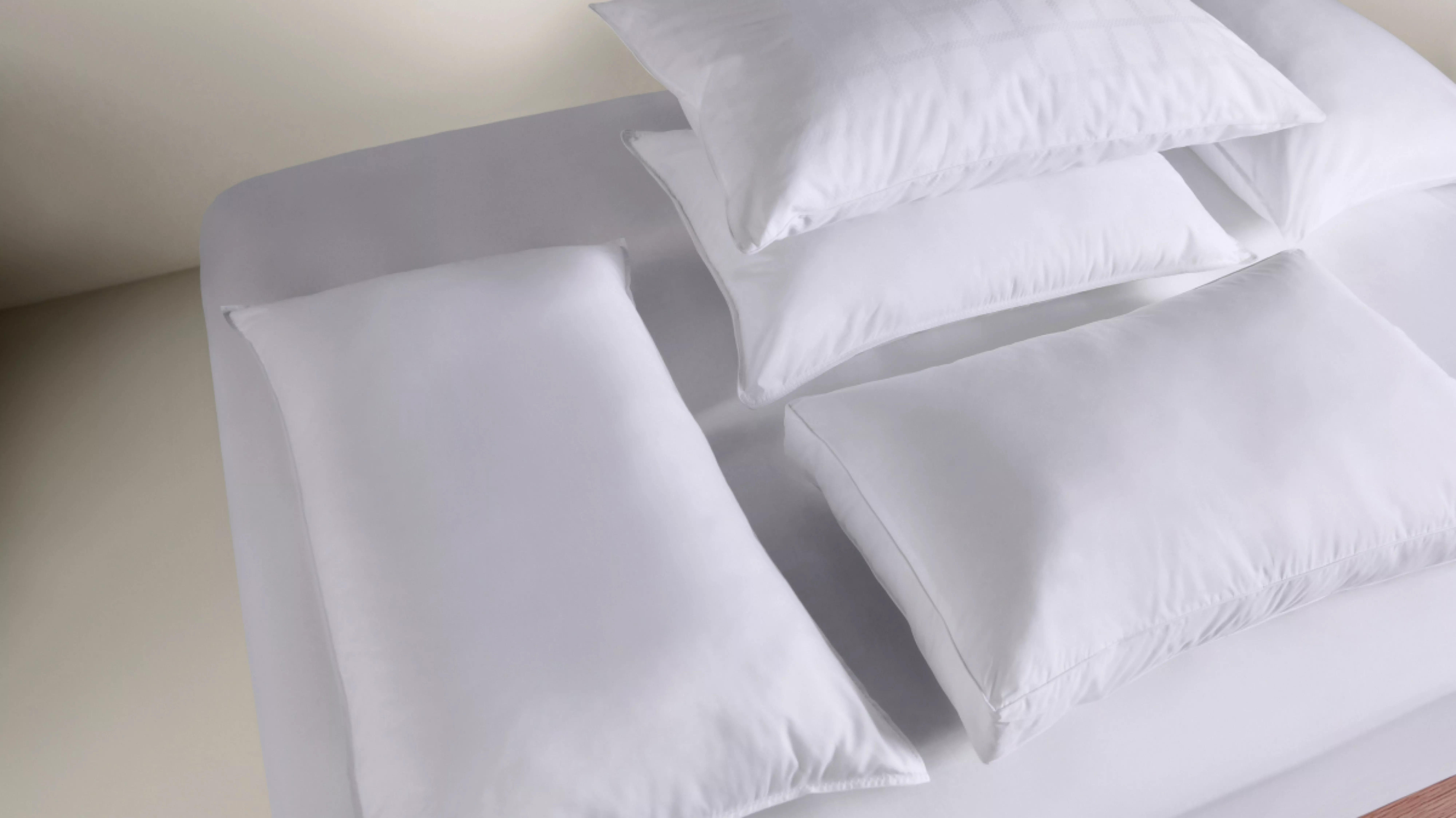 White hotel pillows and long body pillow on a neatly made bed with crisp bedding, close-up bedroom scene