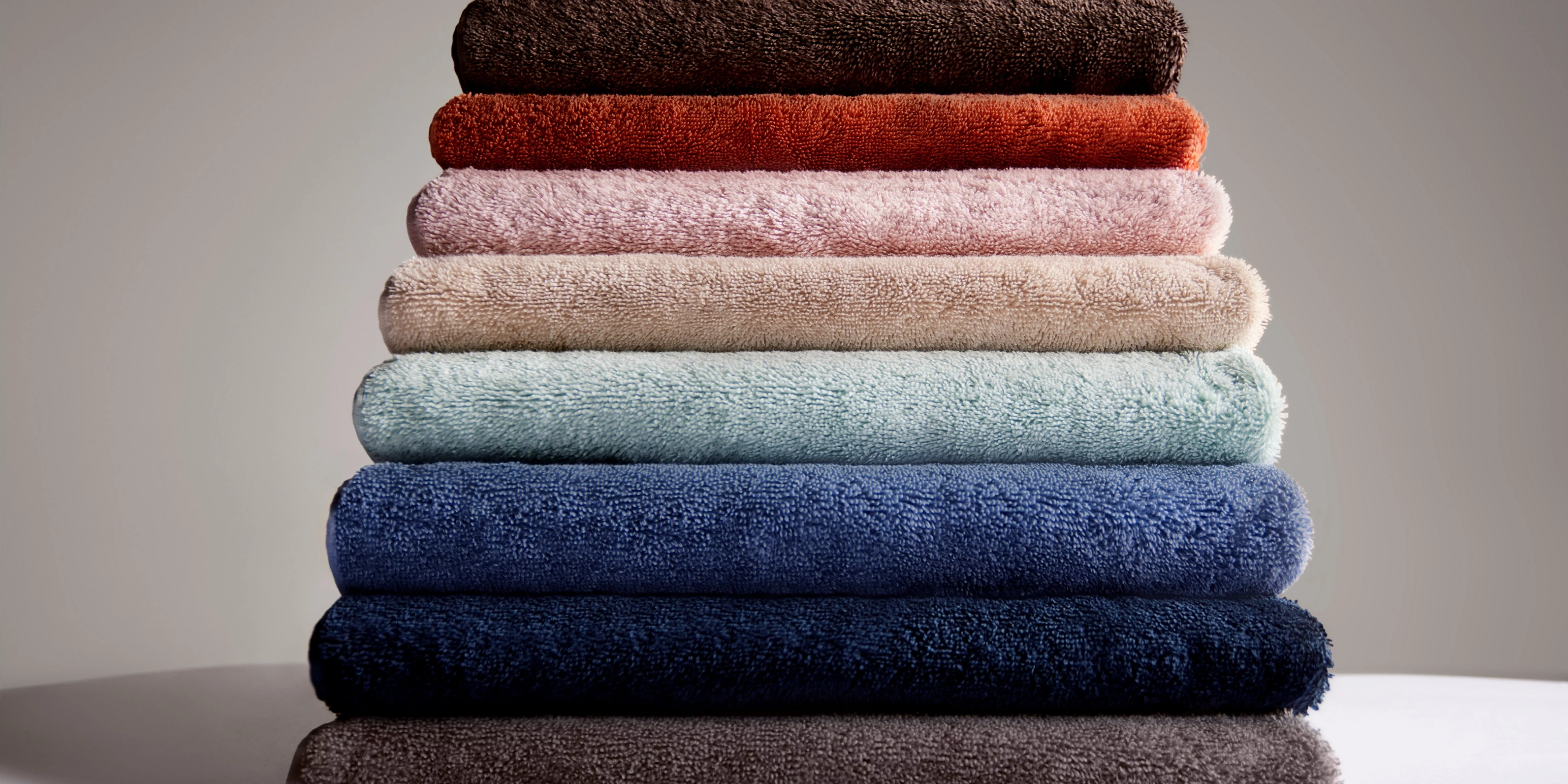 Stack of soft folded bath towels in assorted colours, plush cotton texture, clean bathroom linen display