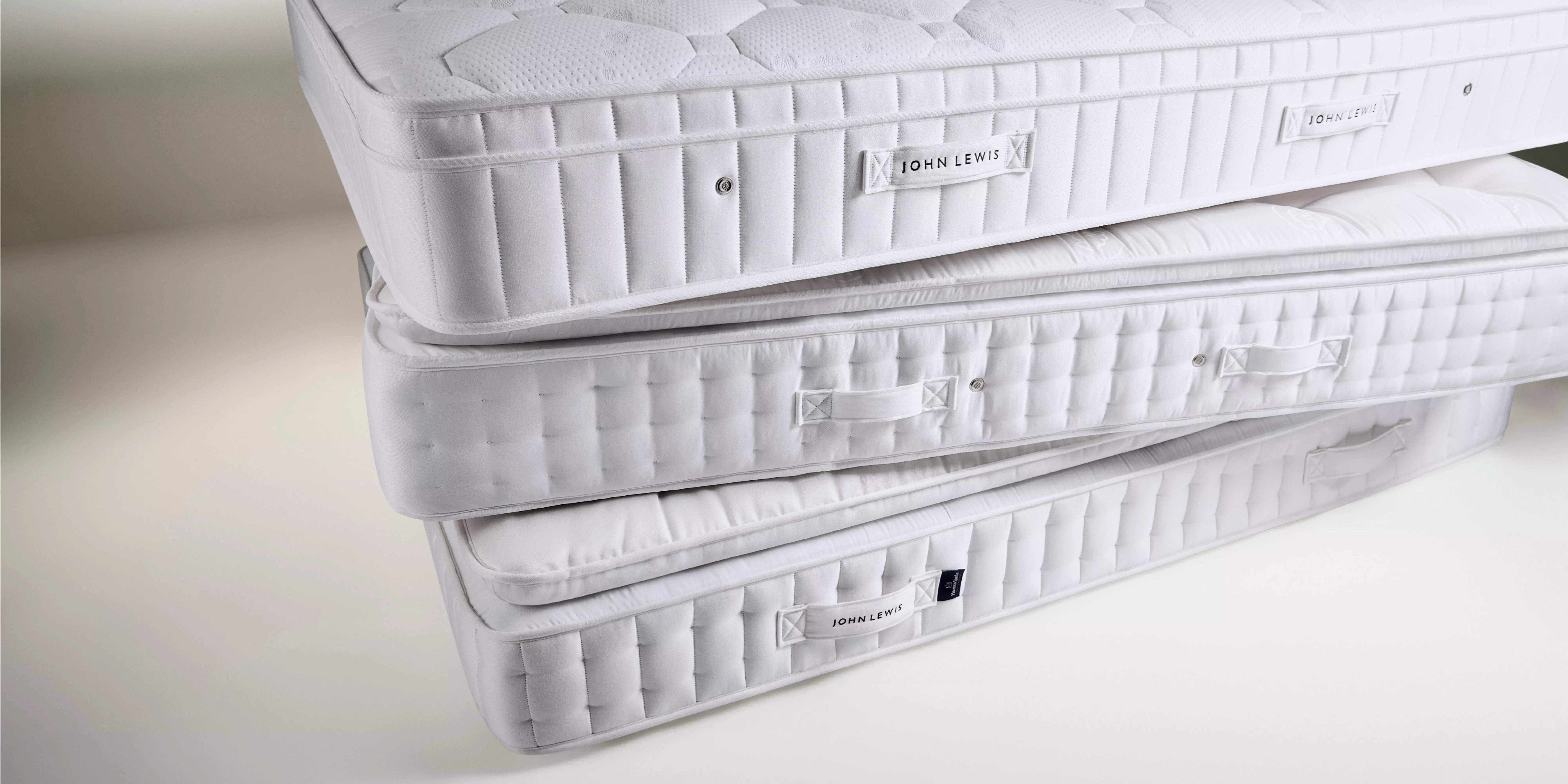 Stacked John Lewis mattresses showing quilted sides and handles, ideal for UK bedroom bedding and sleep comfort.