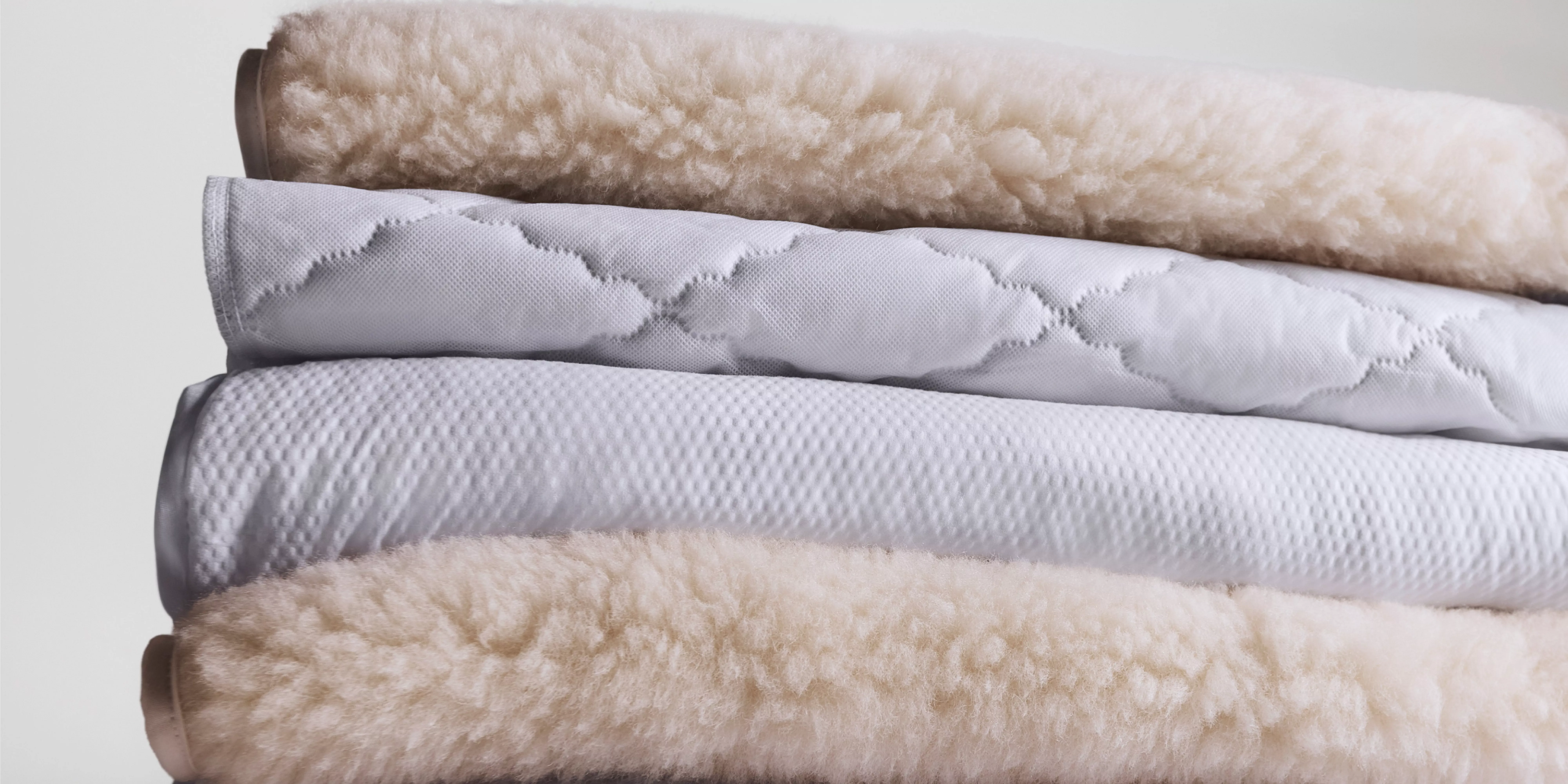 Stacked wool fleece mattress toppers and quilted mattress protector, showing soft breathable bedding layers.