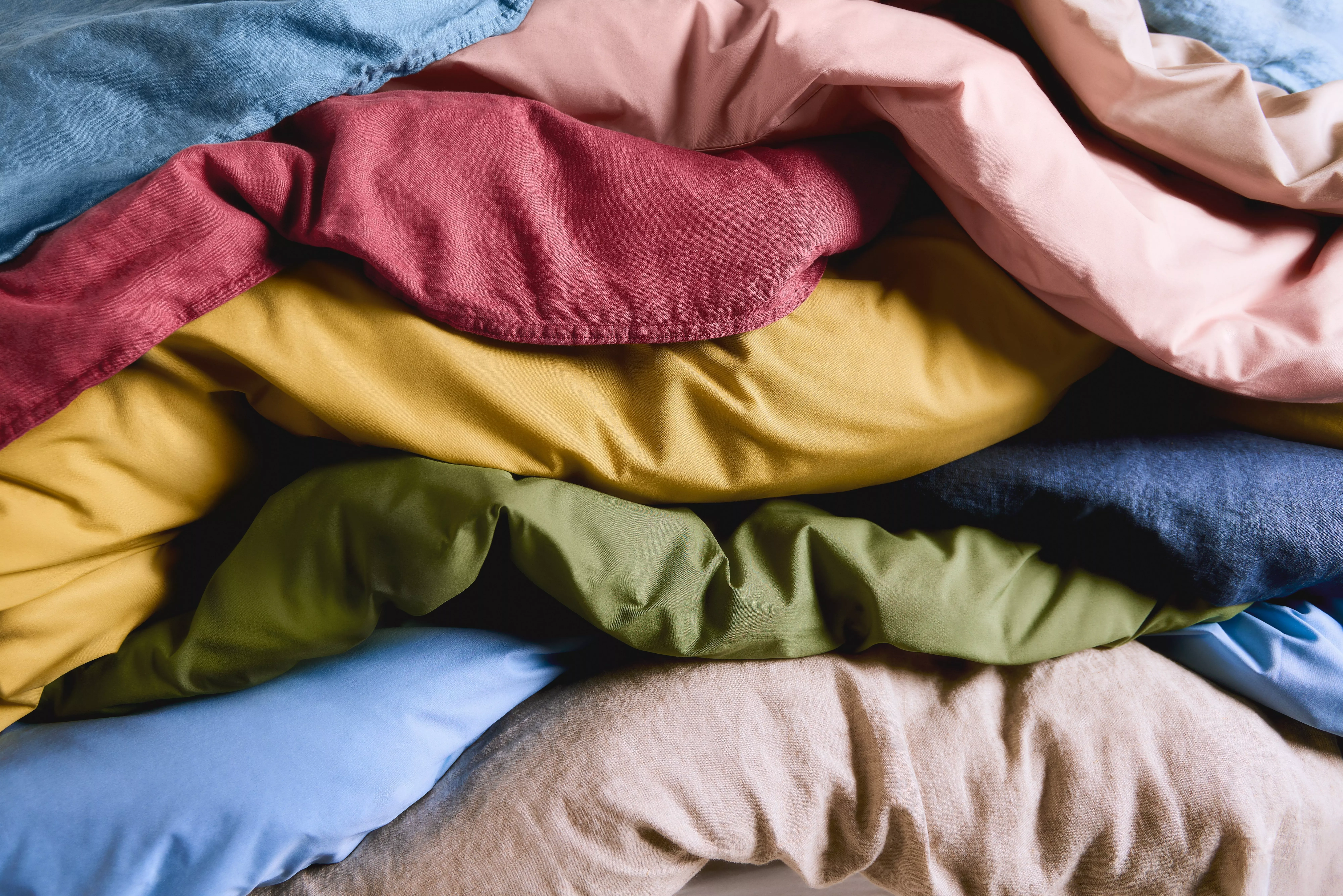 Close-up of colourful linen bedding and duvet covers layered in soft folds, modern bedroom textiles detail