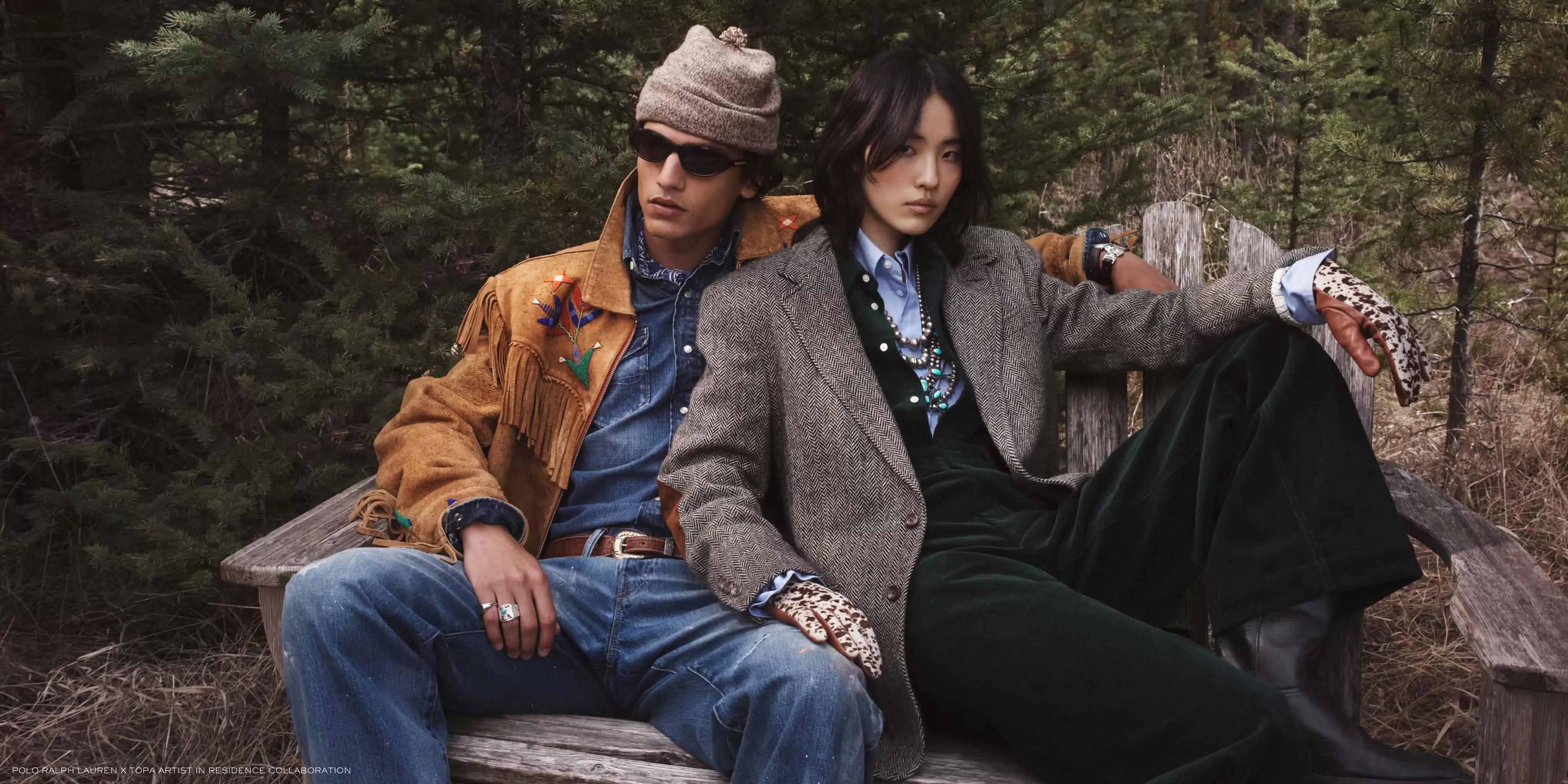 Stylish couple in vintage outdoor fashion on a wooden bench in pine forest, wearing tweed and suede layers