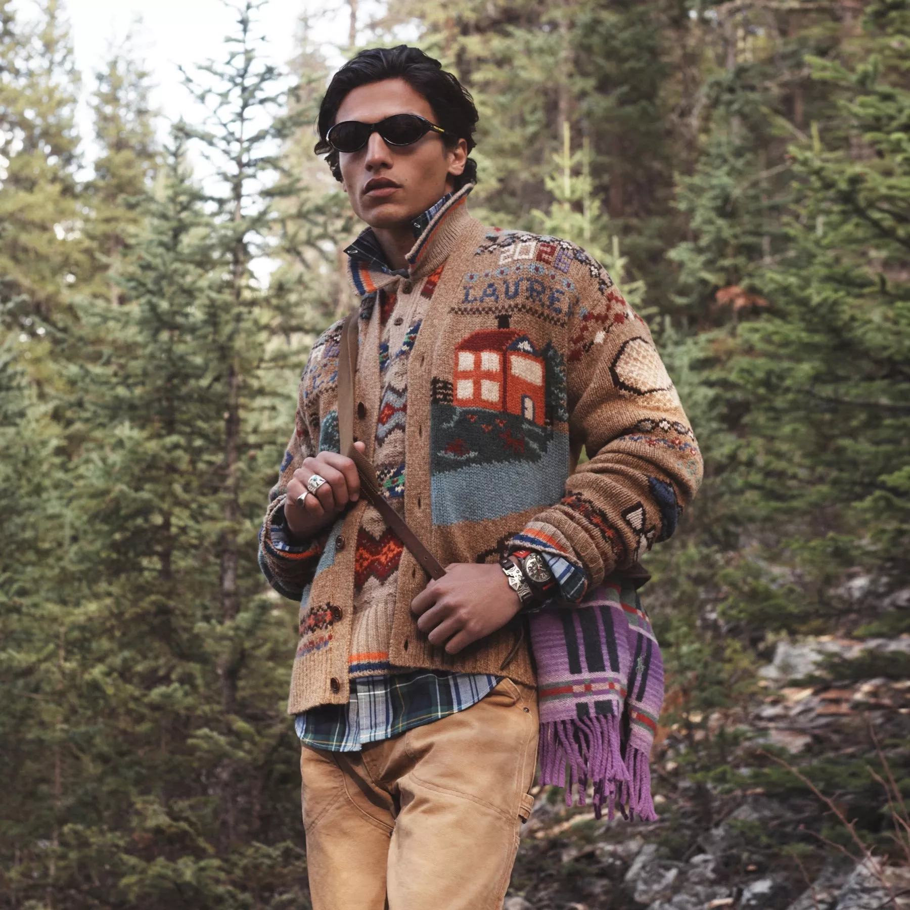 Stylish man in sunglasses wearing patterned knit cardigan in pine forest, outdoor autumn fashion portrait