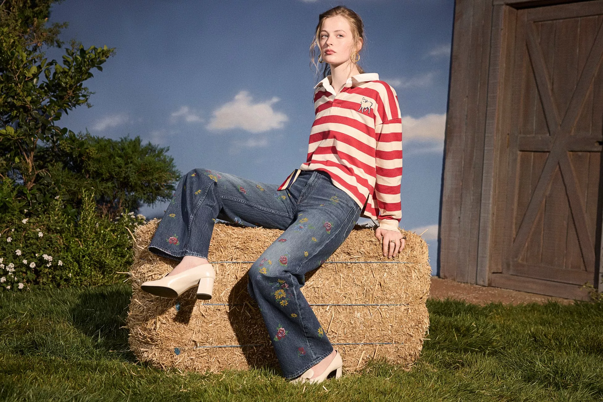 A person wearing a brown polo shirt and blue jeans stands barefoot on a sandy beach against a rocky background.