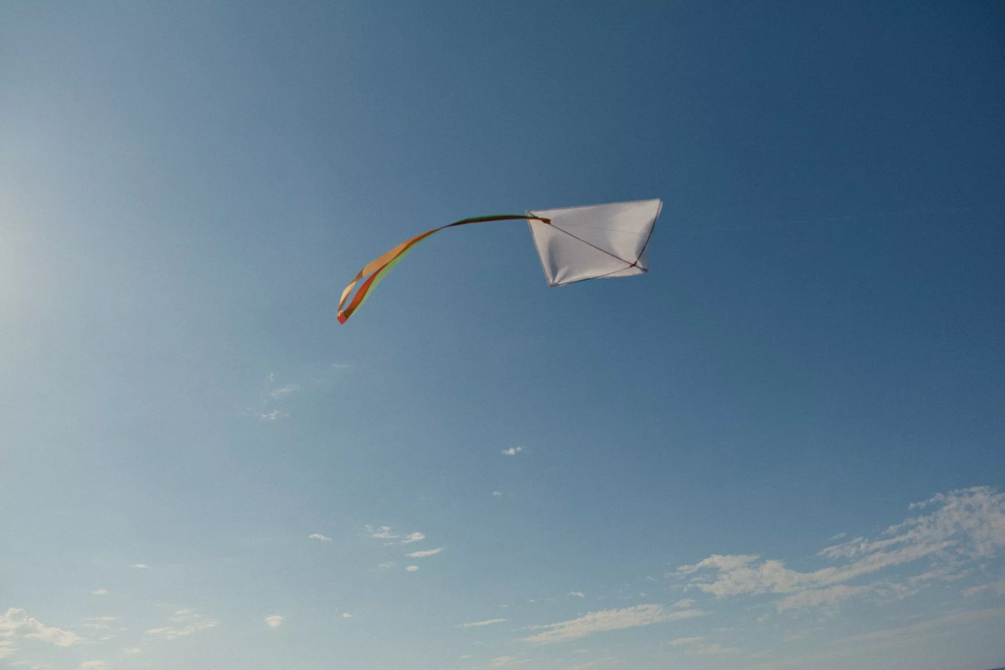 A colourful kite soaring in a clear blue sky with scattered white clouds, symbolising freedom and joy.
