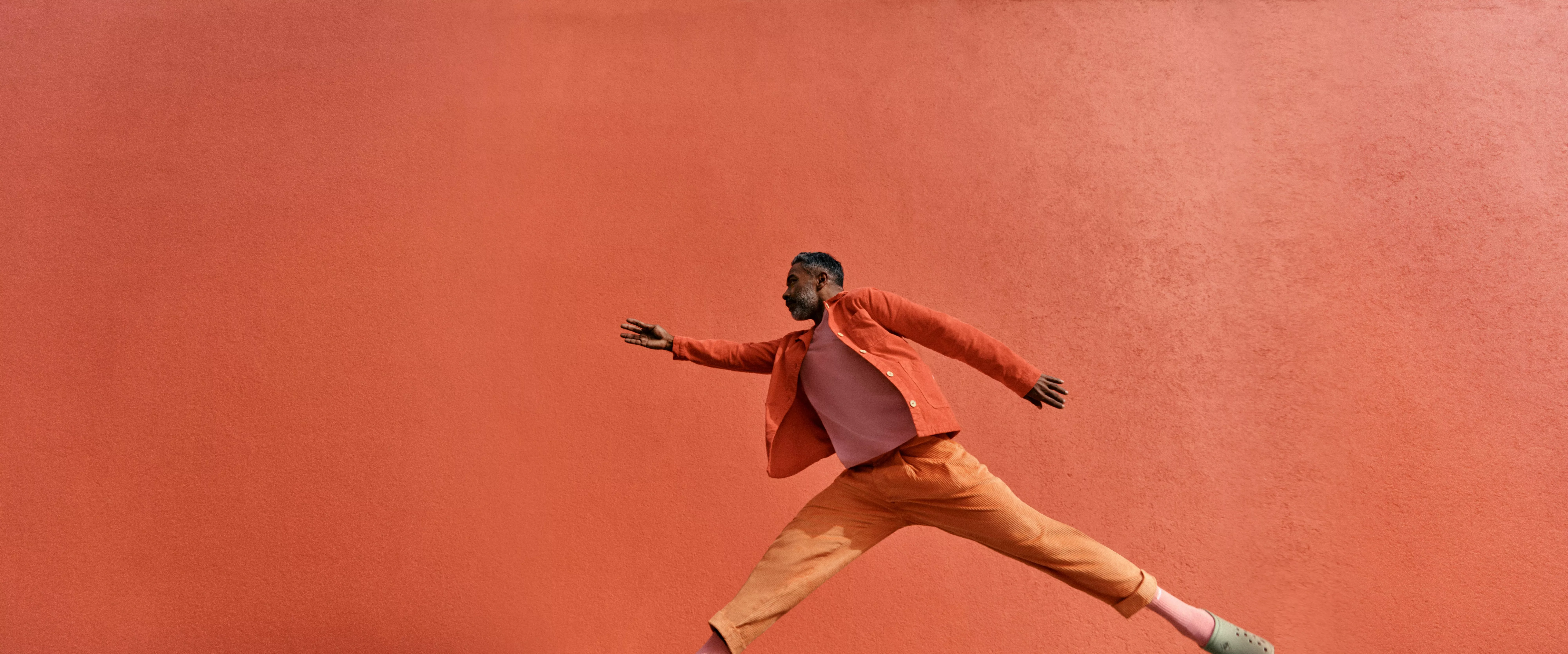 John Lewis Money banner with man running in orange outfit on coral background, promotional advert graphic
