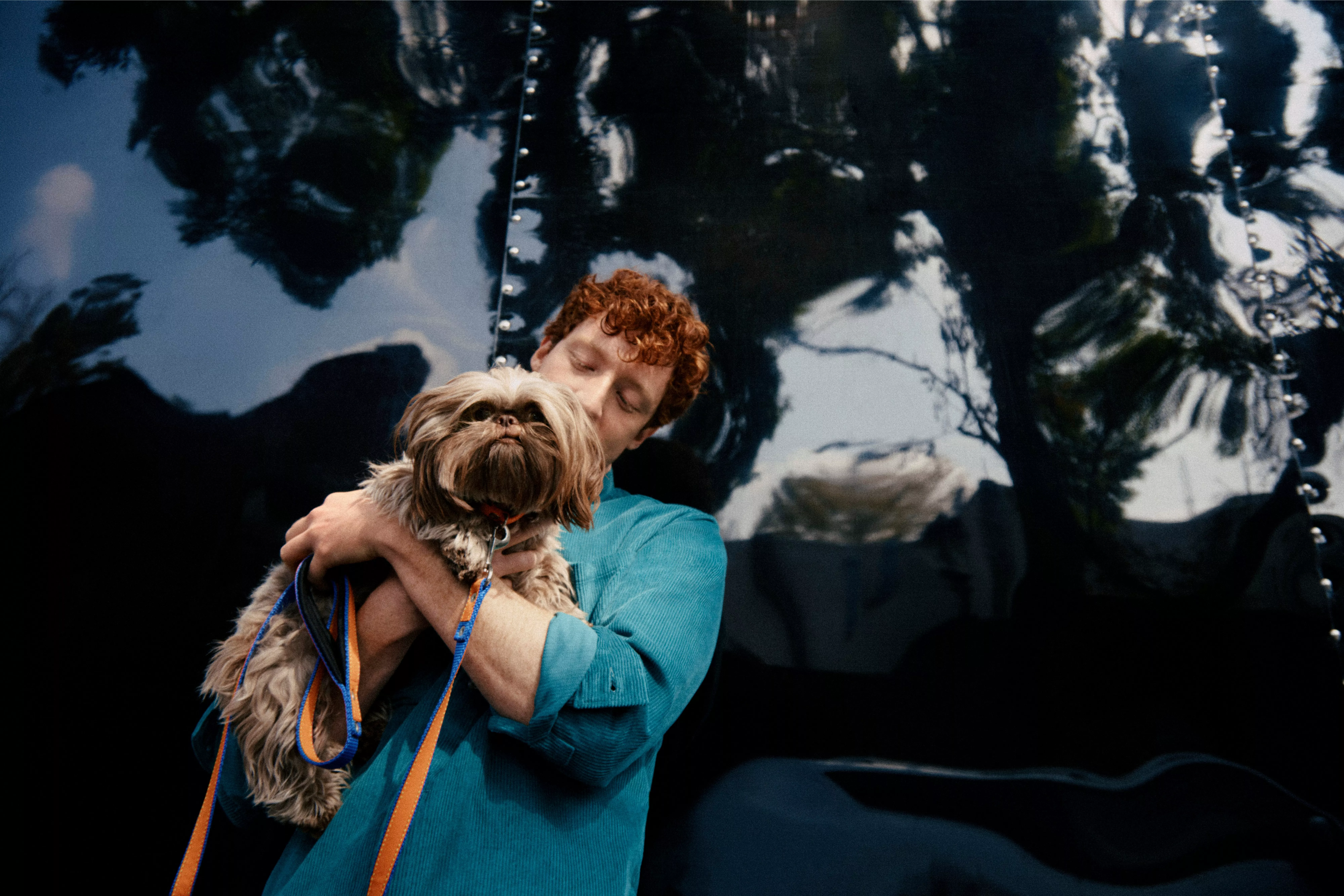 Person holding a small Shih Tzu dog on a lead, outdoor pet portrait with glossy black reflective background