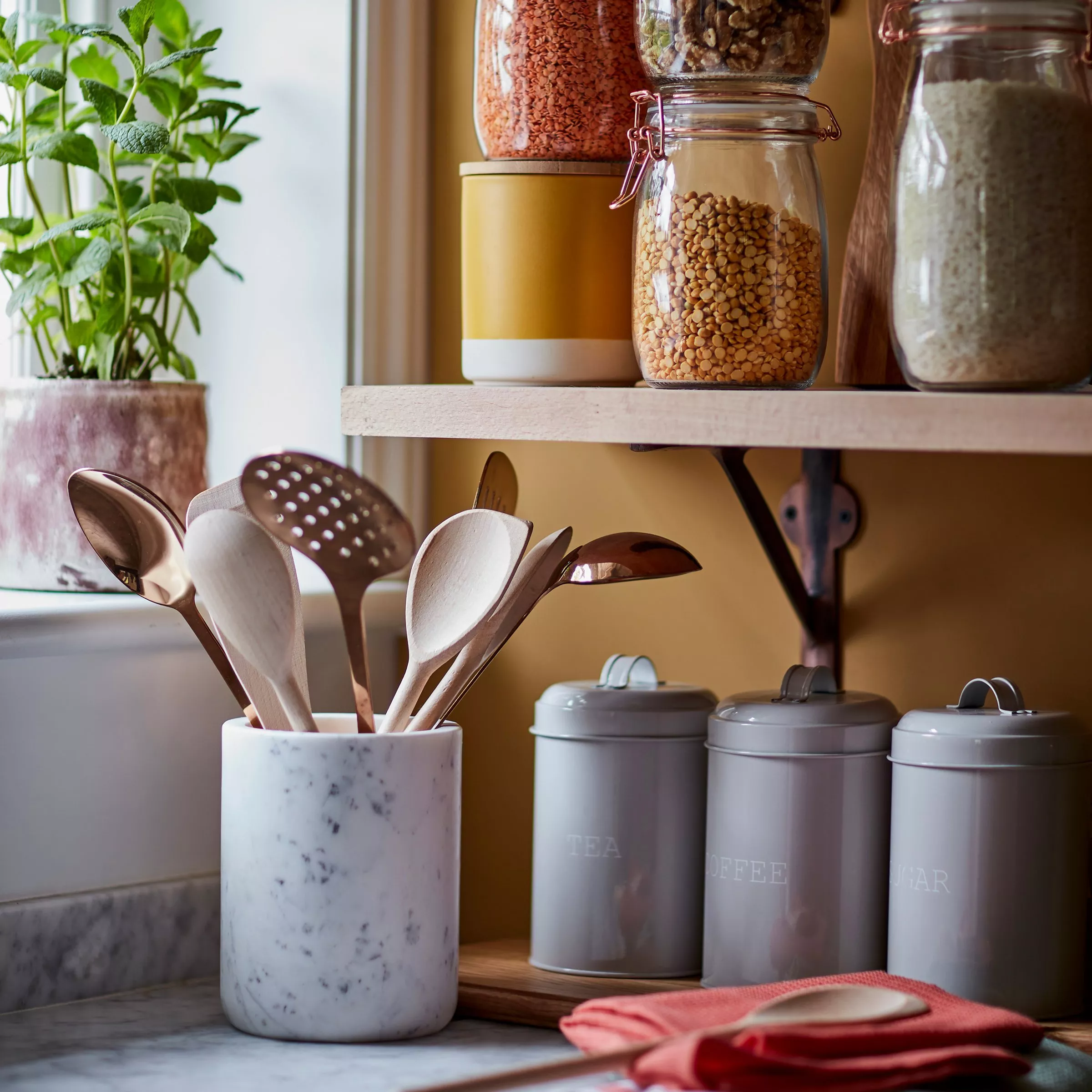 Kitchen countertop storage with glass jars of pulses and grains, utensil pot, and tea, coffee and sugar tins