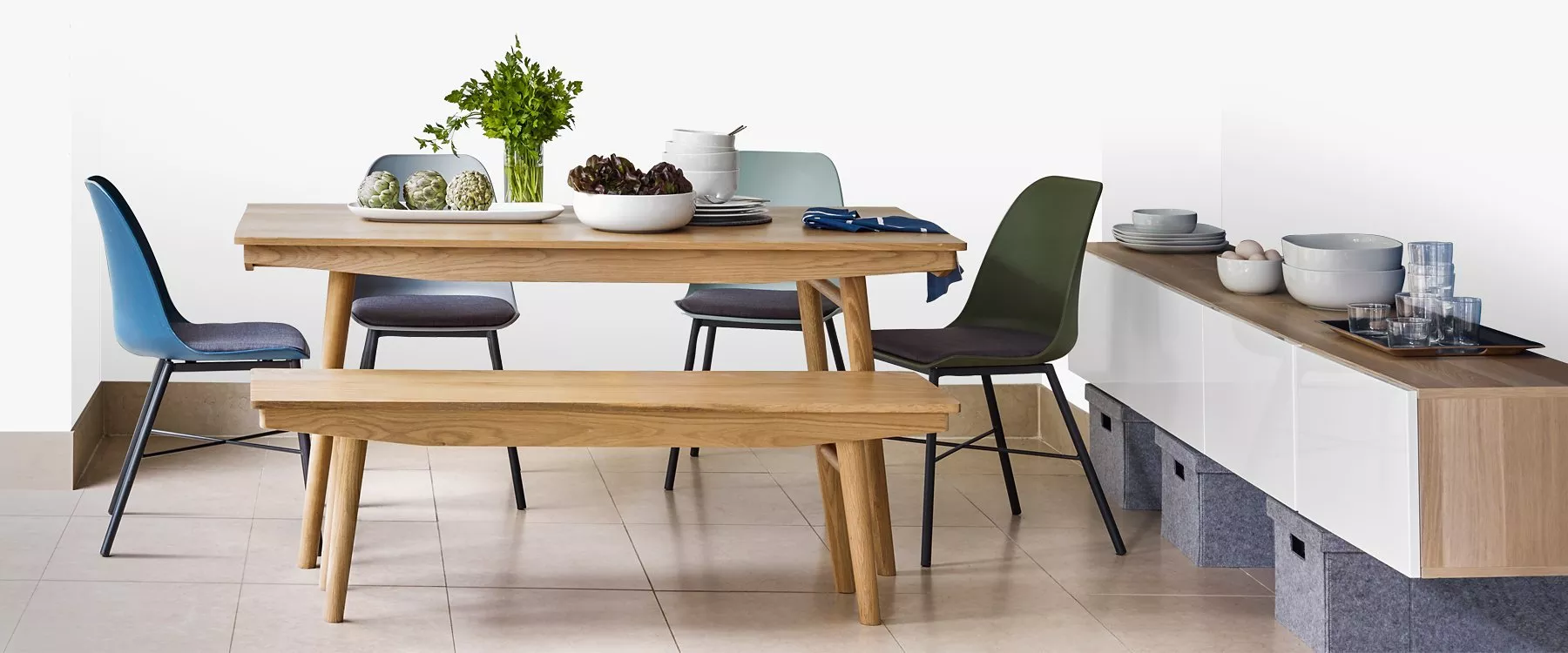 Modern oak dining table with bench and mixed colour chairs, styled with tableware in a bright kitchen setting