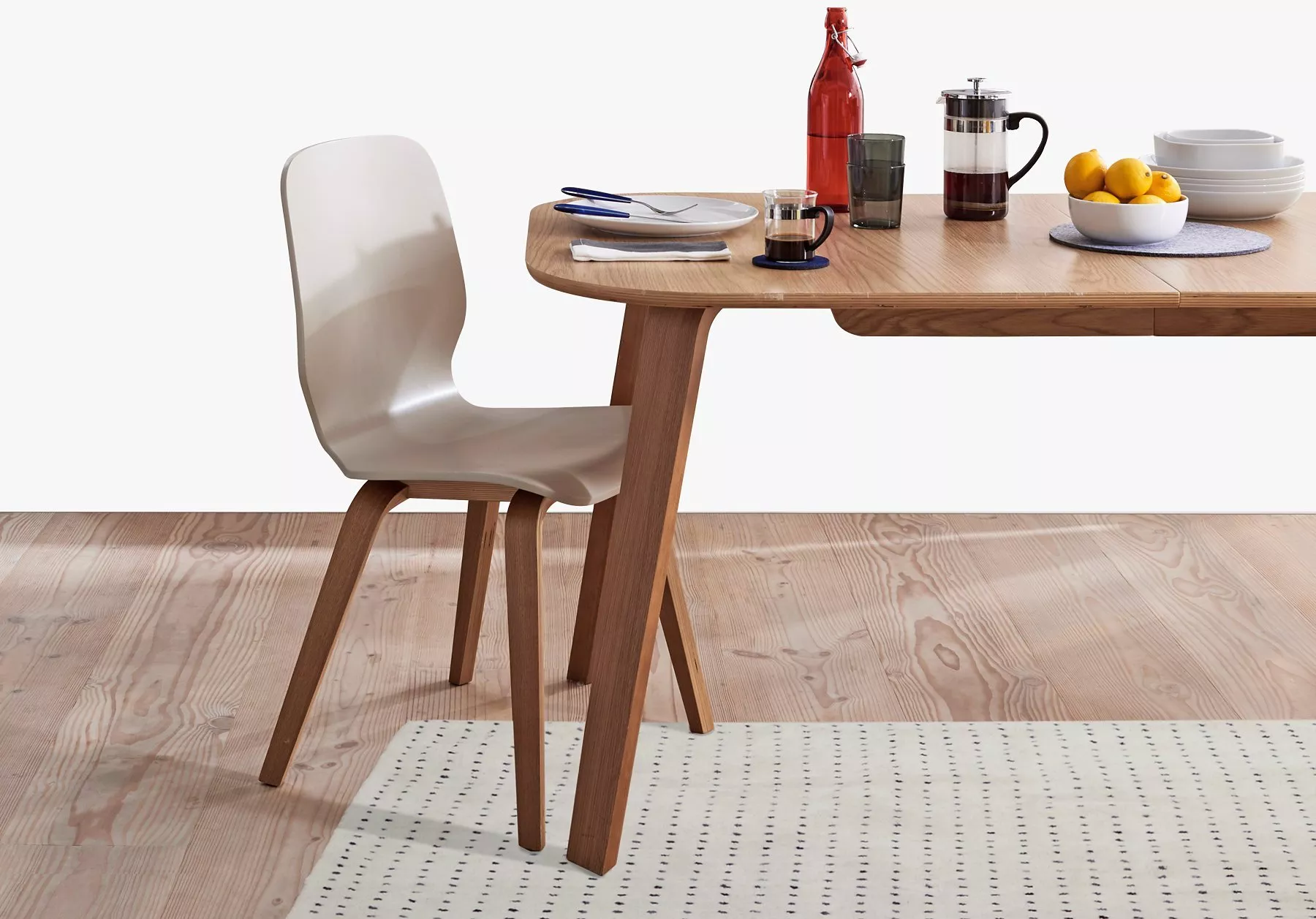 Modern wooden dining table and chair with place settings, coffee press, and bowl of lemons on tabletop
