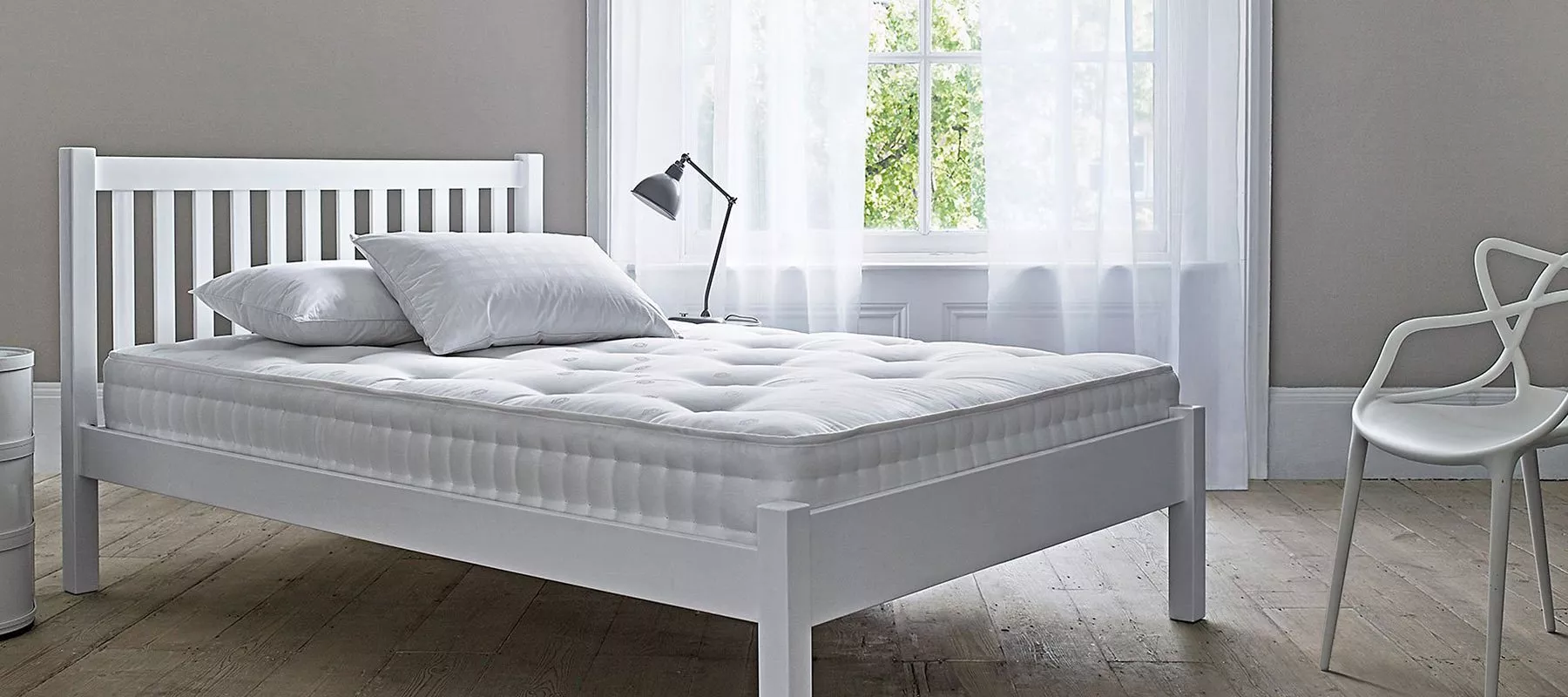 White wooden bed frame with deep quilted mattress and pillows in a bright modern bedroom by a window