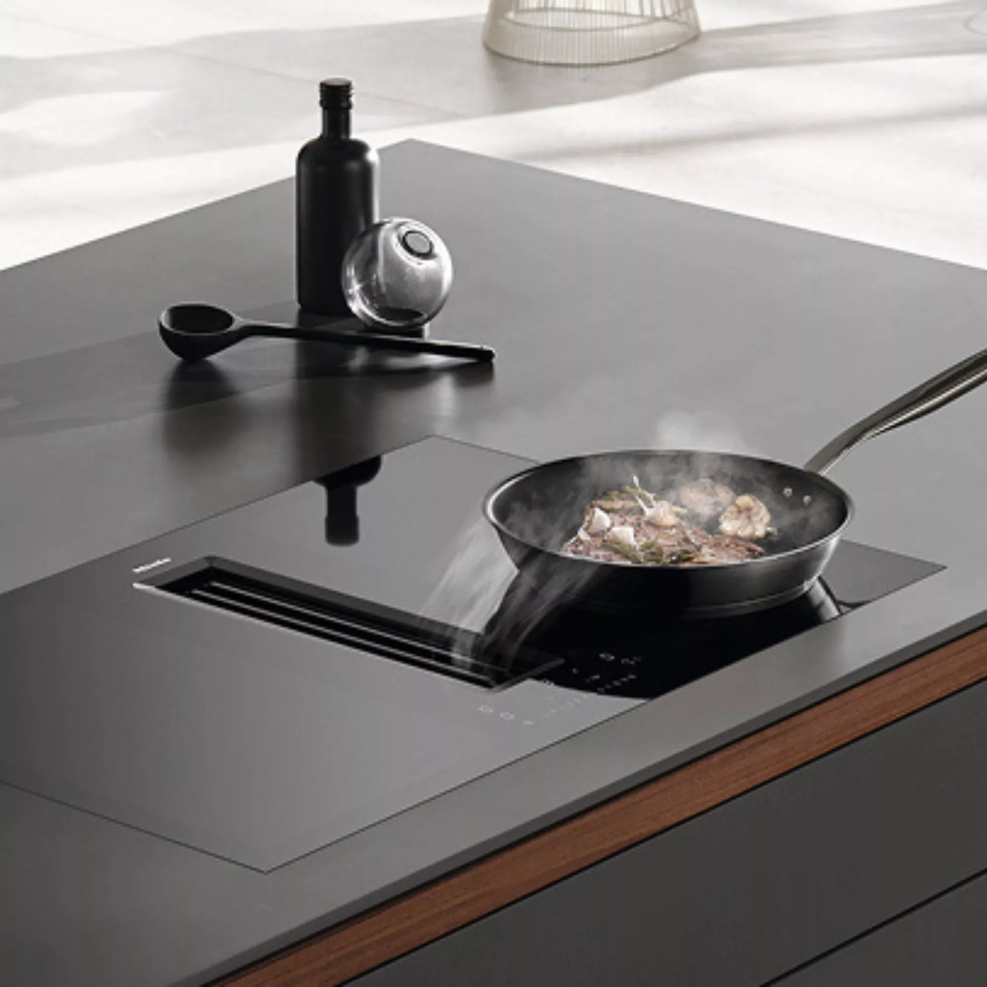 Modern induction hob with built-in downdraft extractor, frying pan cooking food on sleek kitchen worktop