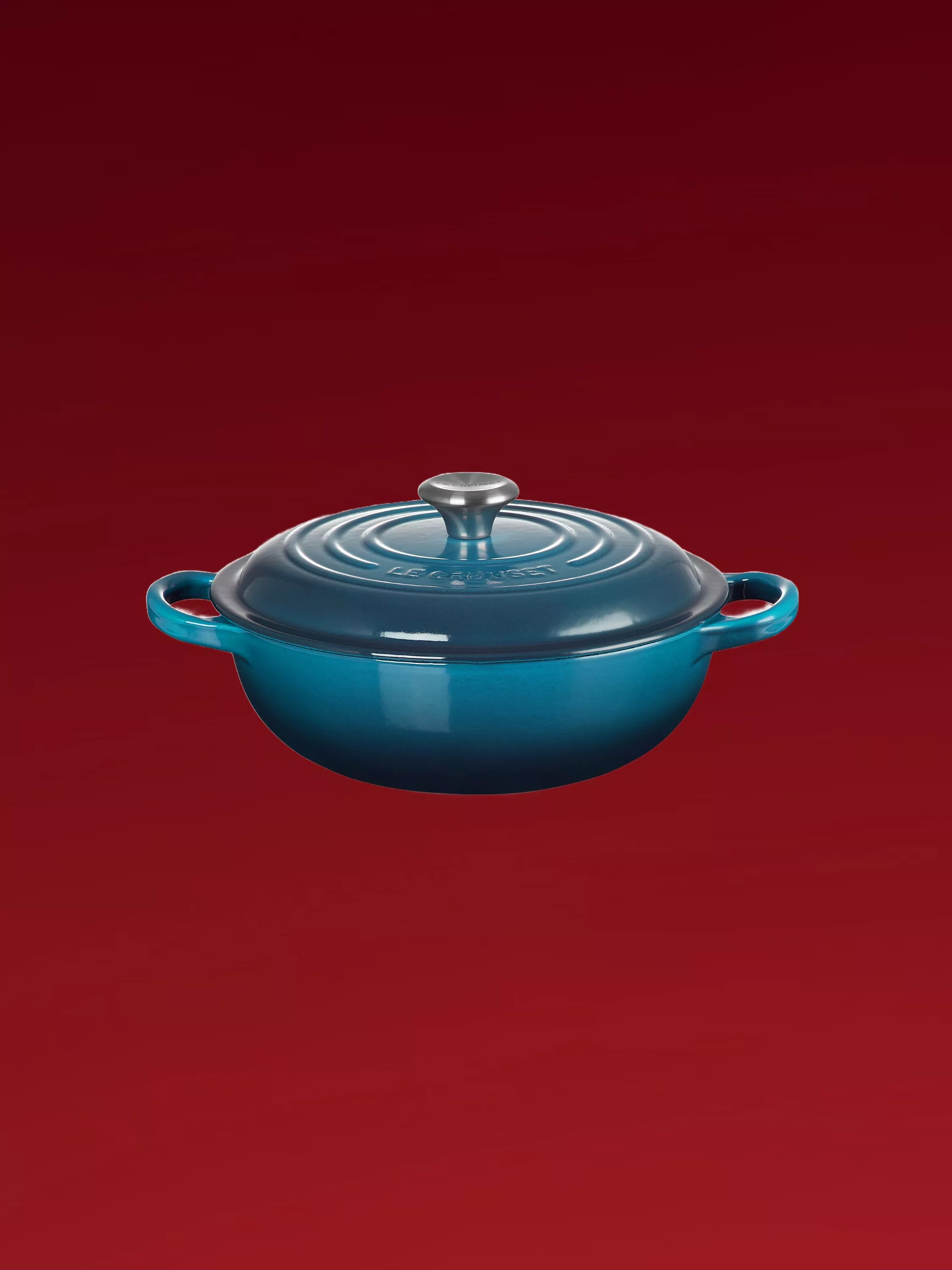 Blue cast iron casserole dish with lid and side handles, isolated on red background for kitchen cookware SEO