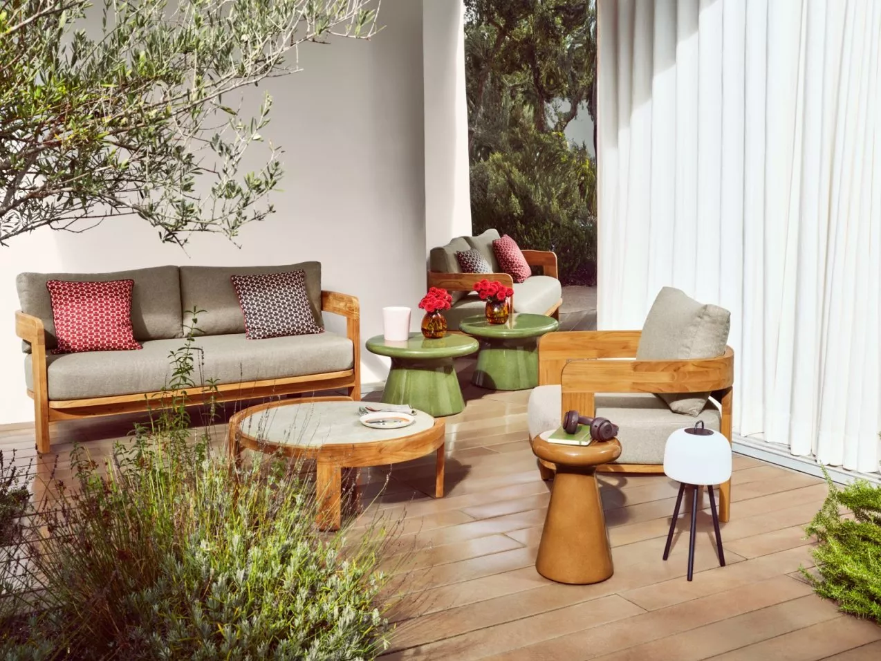 Modern outdoor patio seating with wooden sofa and armchair, green side tables, and cushions by white curtains