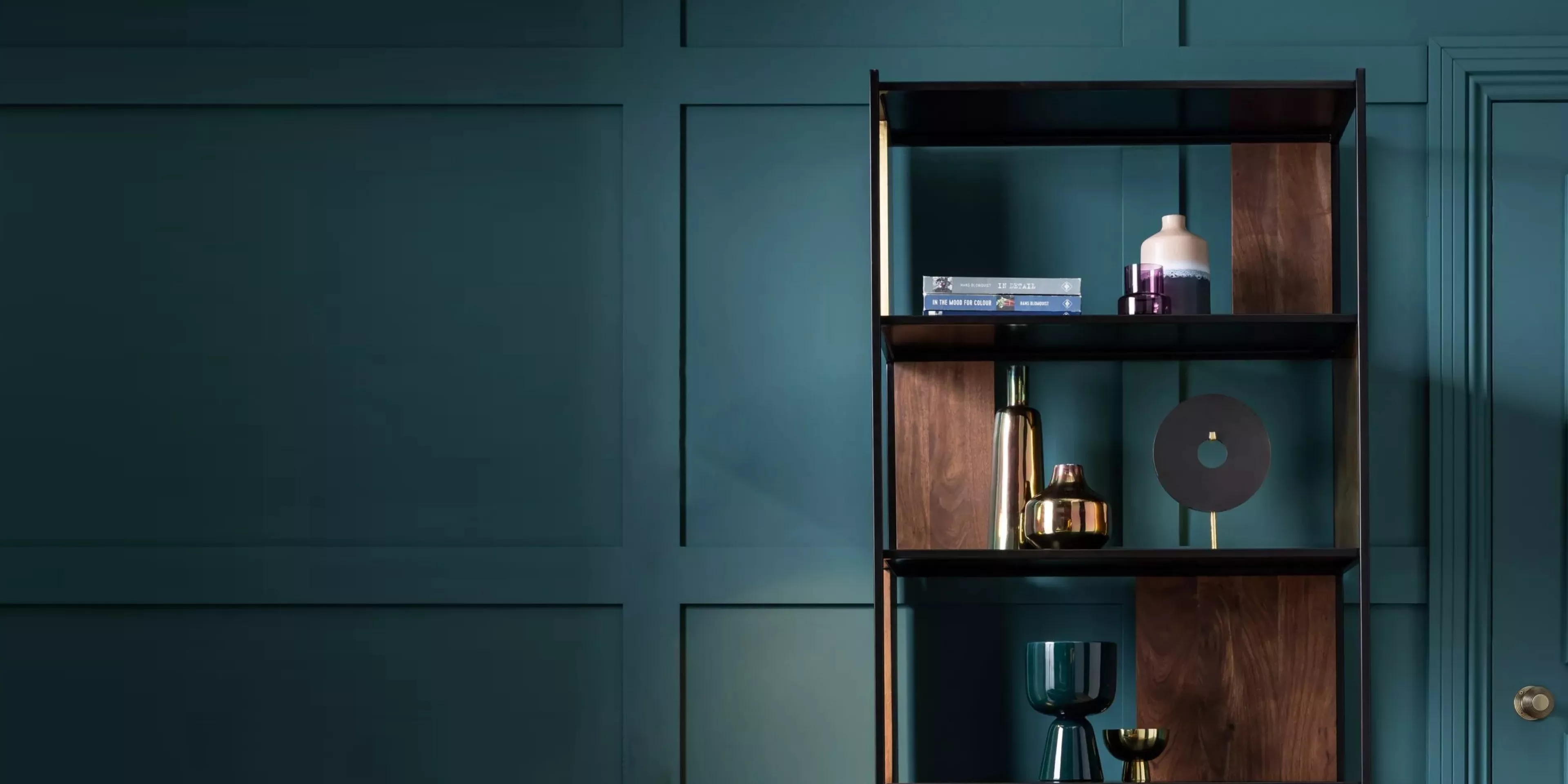 Modern shelving unit with décor and books against teal panelled wall, stylish contemporary interior design scene