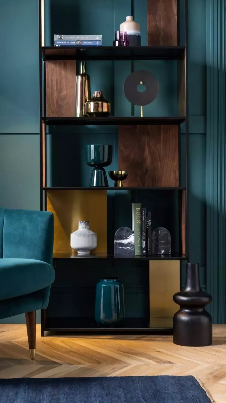Modern open shelving unit with brass accents, vases and books, against teal walls in stylish living room interior.