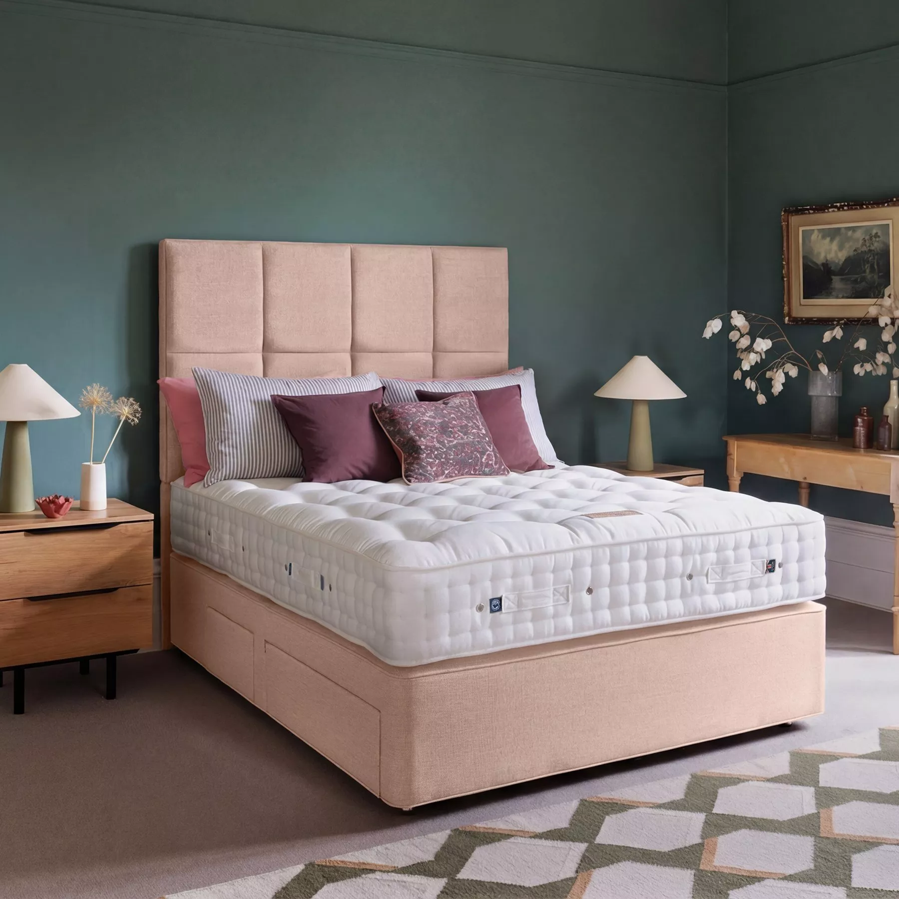 Beige upholstered bed with quilted mattress and mauve cushions in modern bedroom with wooden bedside tables