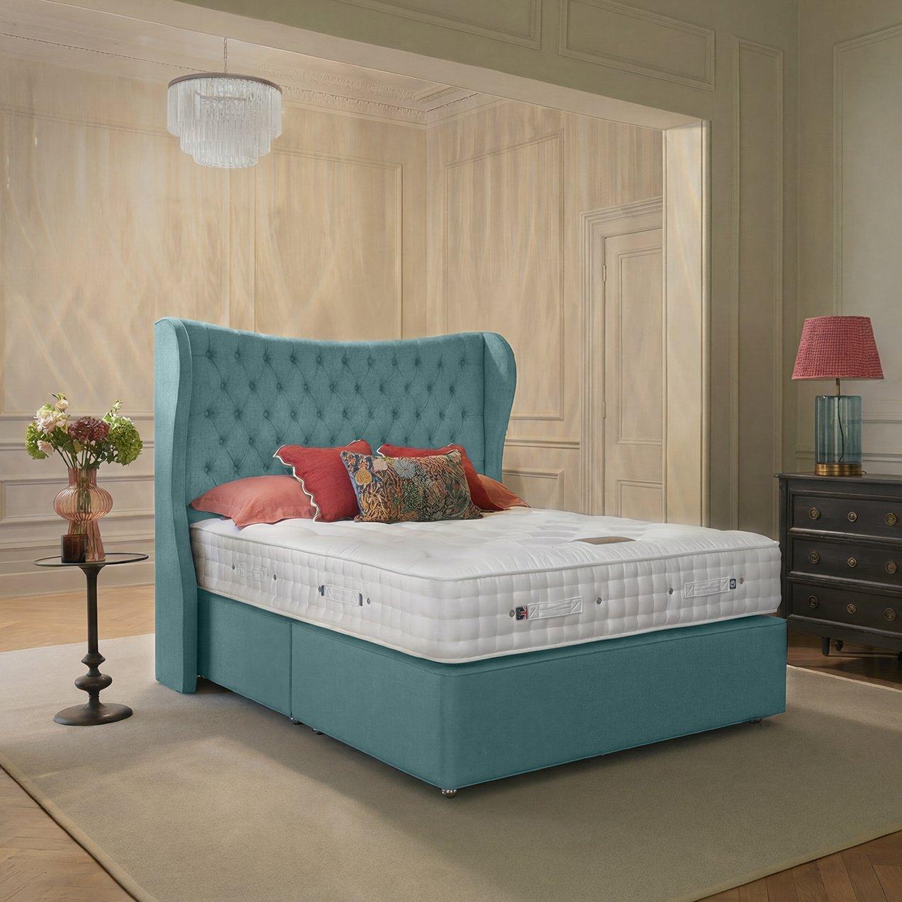 An upholstered teal wingback bed with a button-tufted headboard, dressed in a thick white tufted mattress, red decorative pillows, and a pattern-patterned accent cushion in an elegant bedroom setting.
