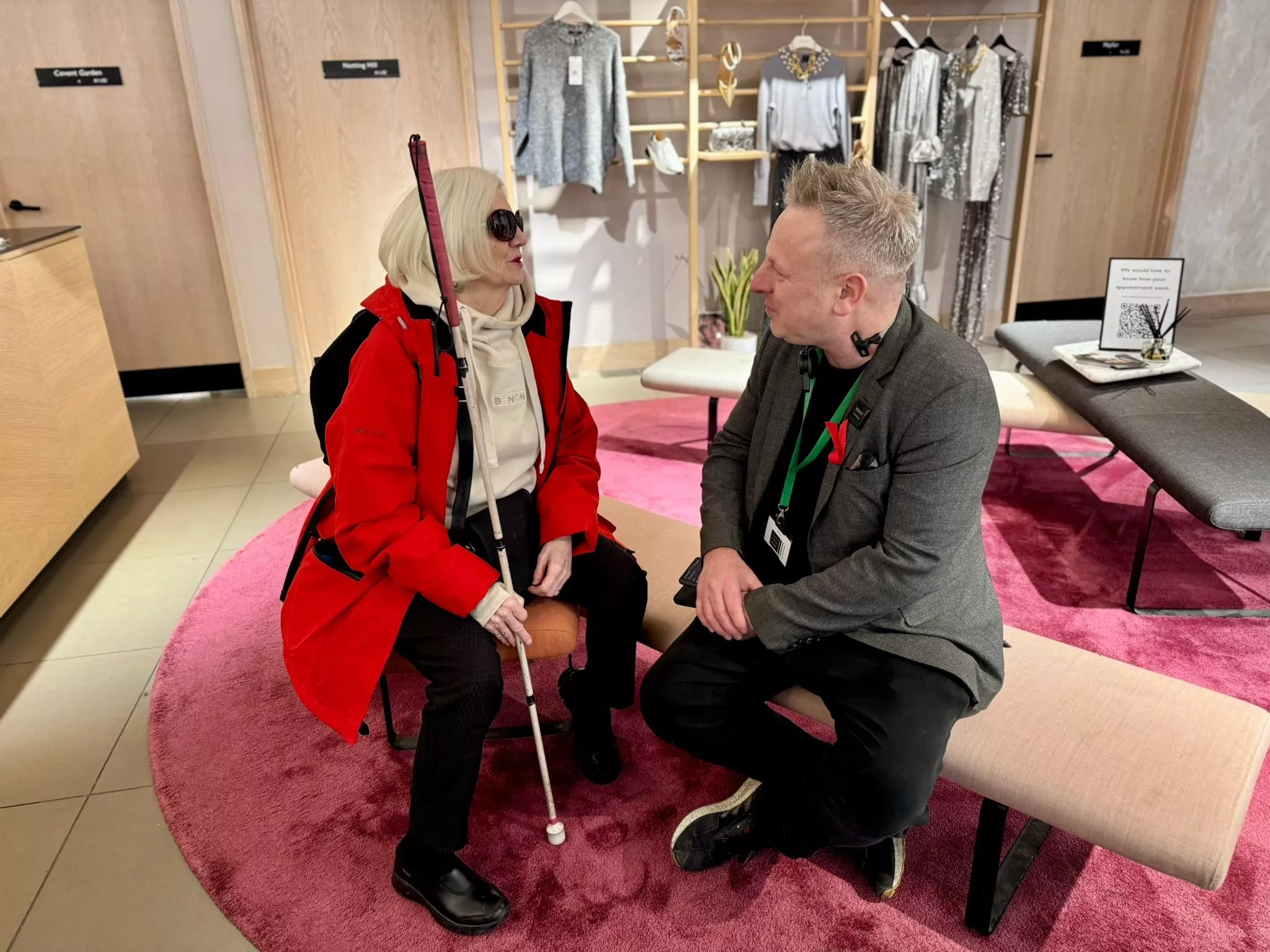 Shop assistant speaking with a visually impaired customer in a modern clothing store seating area
