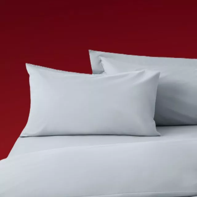 Light grey bed linen set with pillowcases on a bed, photographed against a bold red background backdrop