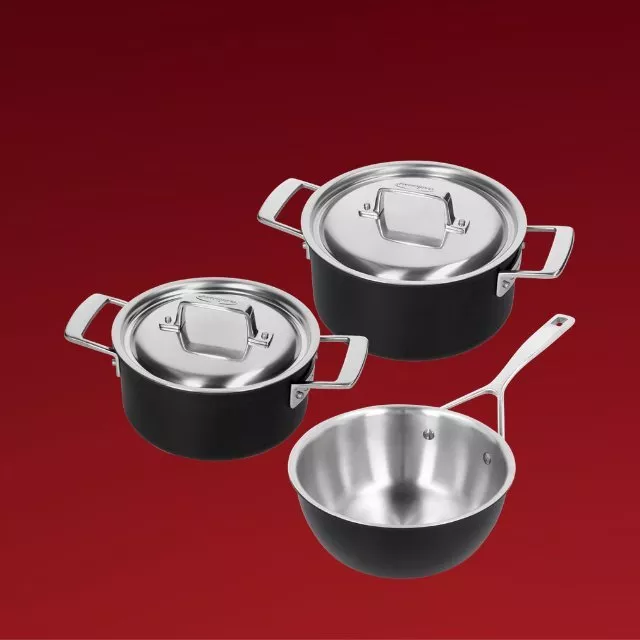 Three-piece stainless steel saucepan set with lidded pots and sauté pan, black exterior on red background