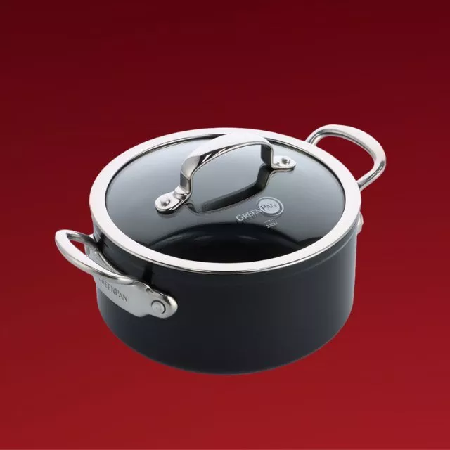 Black non-stick casserole pot with glass lid and stainless steel handles on a red background, cookware product photo
