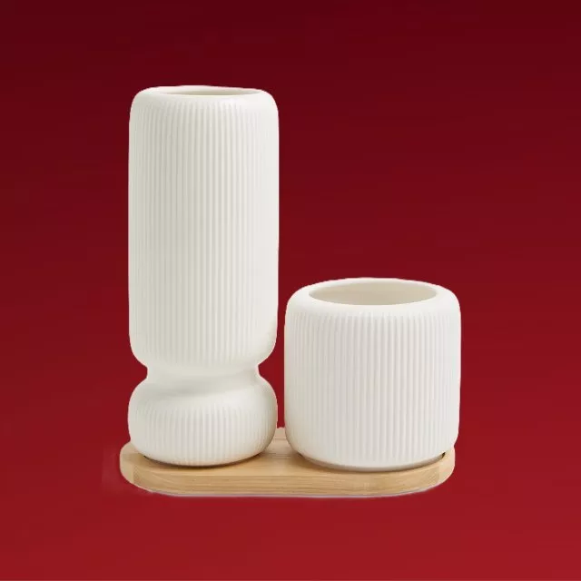 Modern white ribbed ceramic vase and candle holder set on wooden tray against deep red background