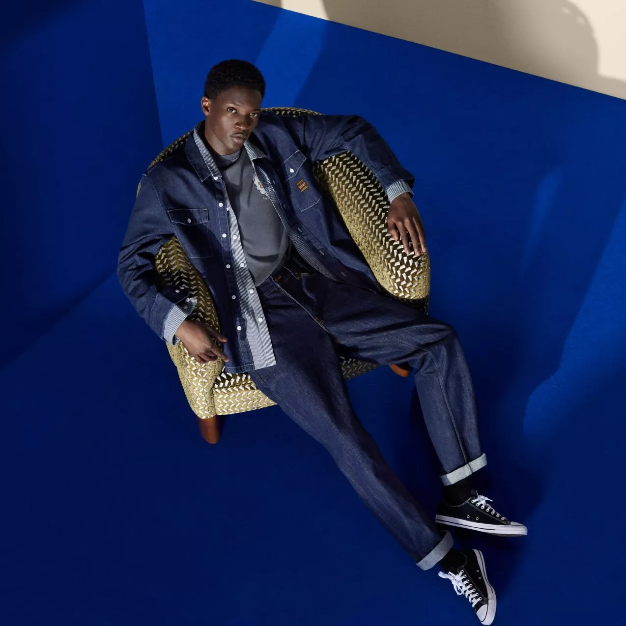 Menswear model in dark denim jacket and jeans posing against bold orange studio backdrop, modern fashion shoot