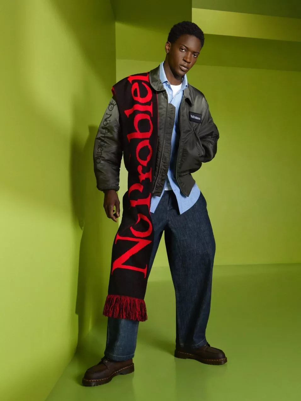 Fashion model in bomber jacket, blue shirt and jeans, wearing bold red-and-black scarf in green studio set