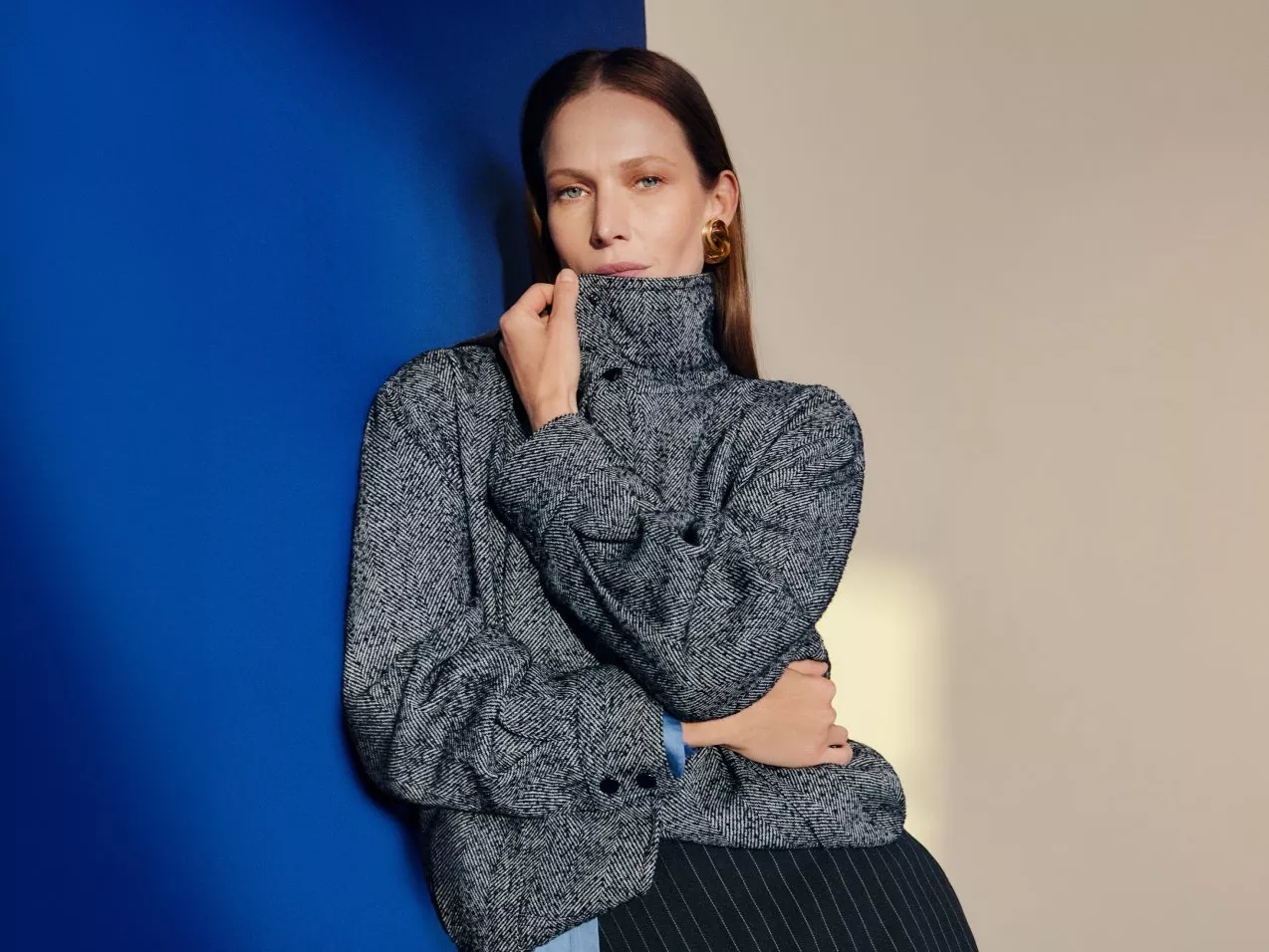 Fashion portrait of woman in grey tweed high-neck jacket, posing against blue and beige studio backdrop