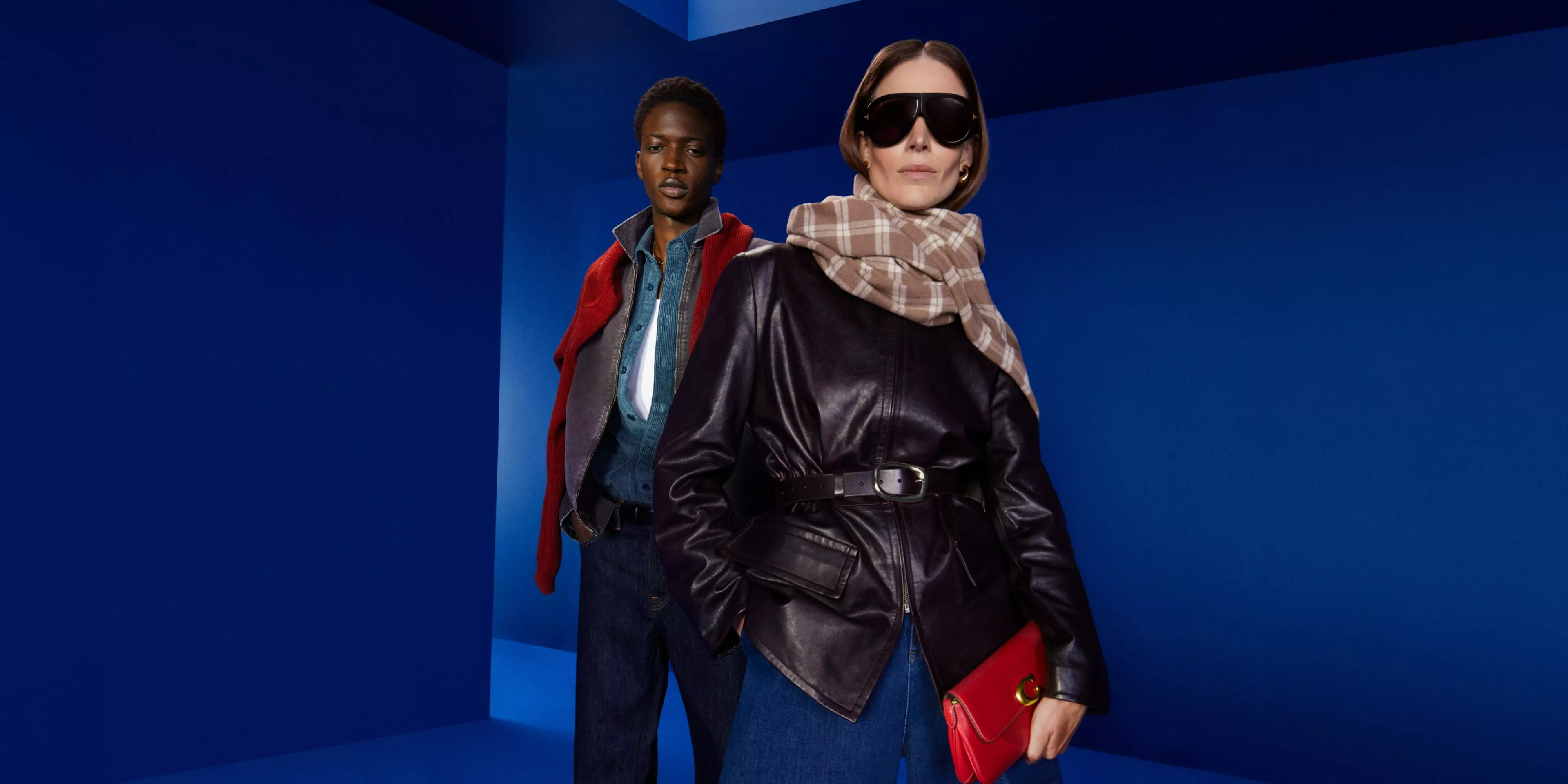Fashion models in blue studio wearing leather jacket, checked scarf and sunglasses, holding red handbag