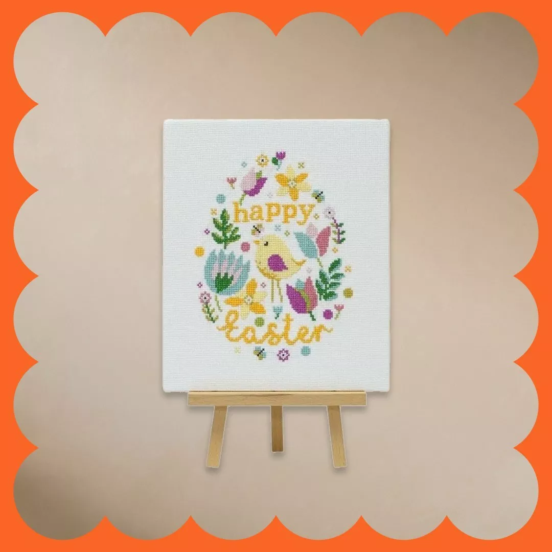 Easter-themed embroidery featuring flowers and birds on a canvas. Displayed on a small wooden easel.