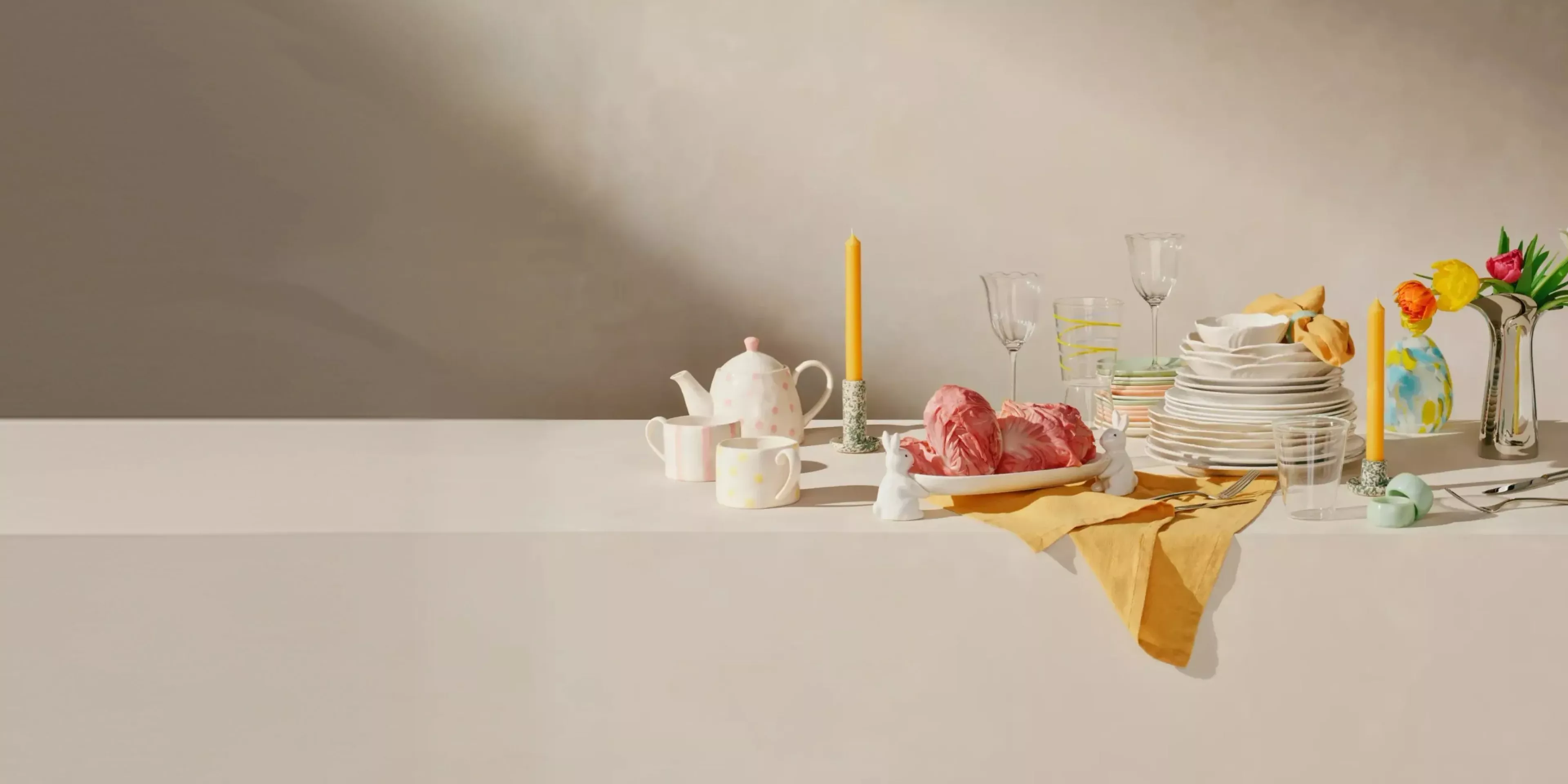 Elegant table setting with a teapot, candles, and vibrant flowers; a stack of plates adds to the aesthetic.