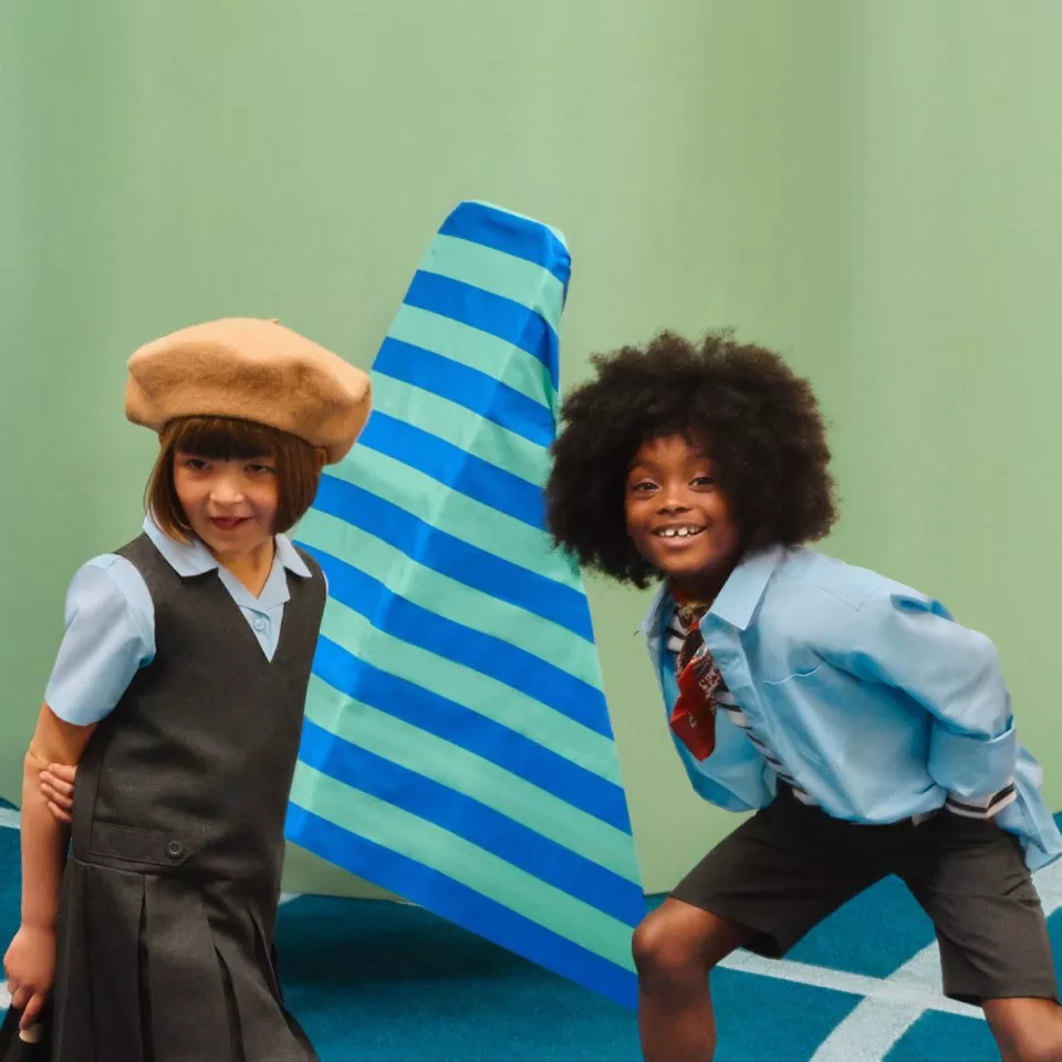 Two primary school children posing by a blue striped surfboard in a studio, wearing retro school uniforms.