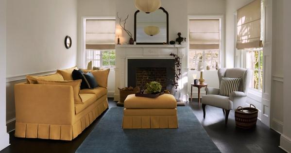 Bright modern living room with mustard sofa, striped armchair, blue rug and white fireplace mantelpiece
