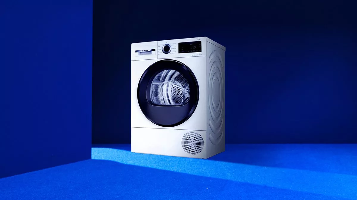 White front-loading tumble dryer in blue studio, modern energy-efficient laundry appliance with digital controls