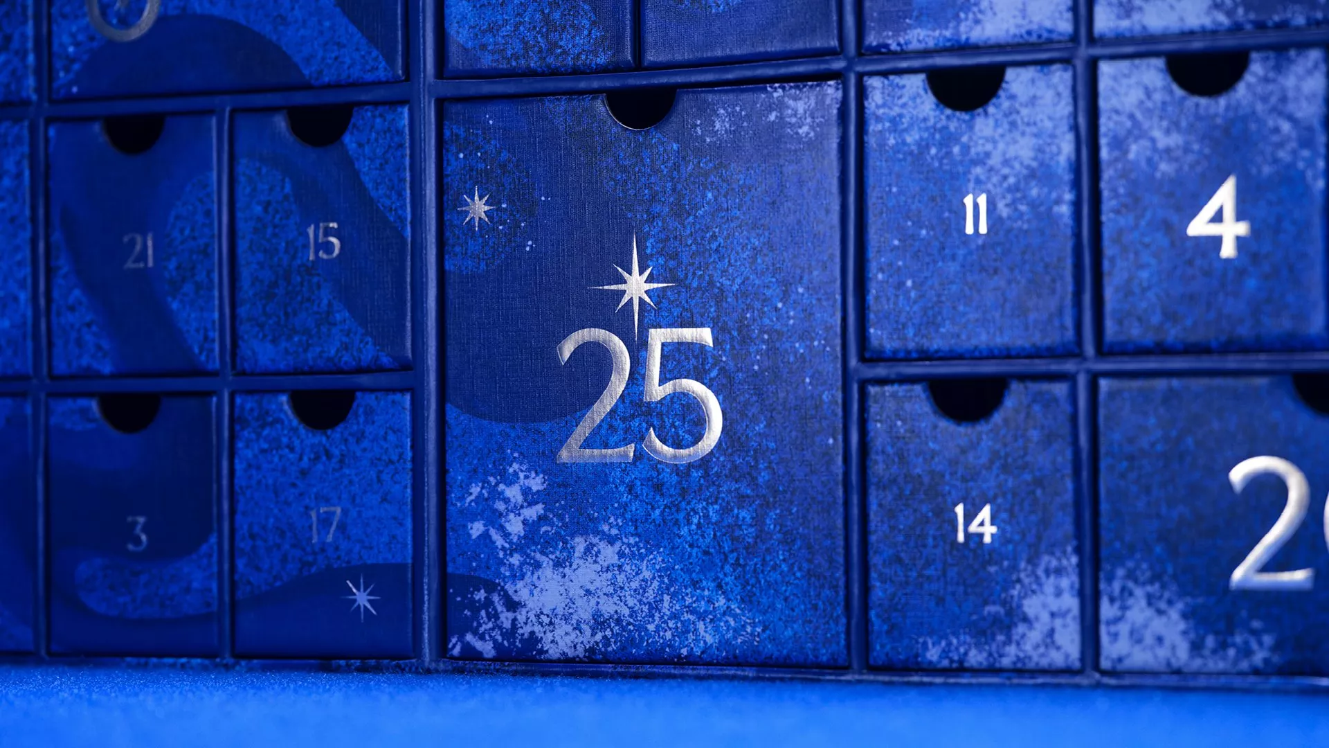 Blue advent calendar close-up with numbered doors, featuring 25 in silver and festive star details on boxes