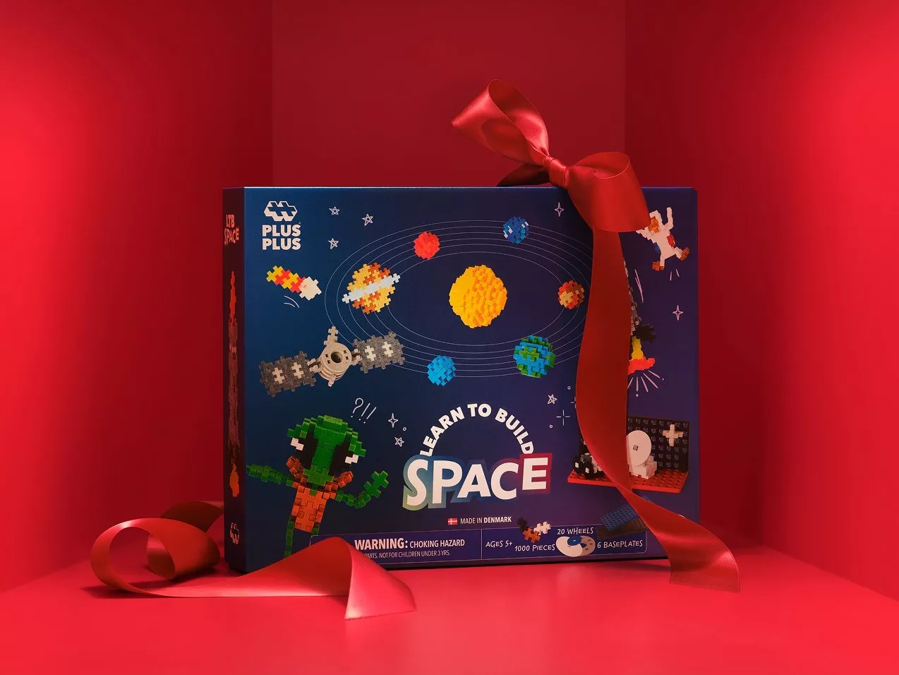 Plus-Plus Learn to Build Space construction toy set gift box with red ribbon bow on red background