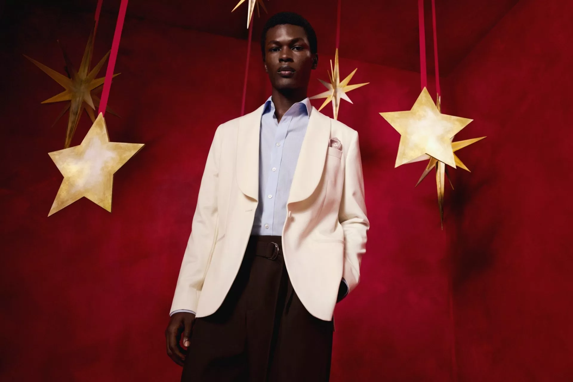 Male model wearing a bomber jacket over a blue striped shirt and wide-leg jeans against a green studio backdrop