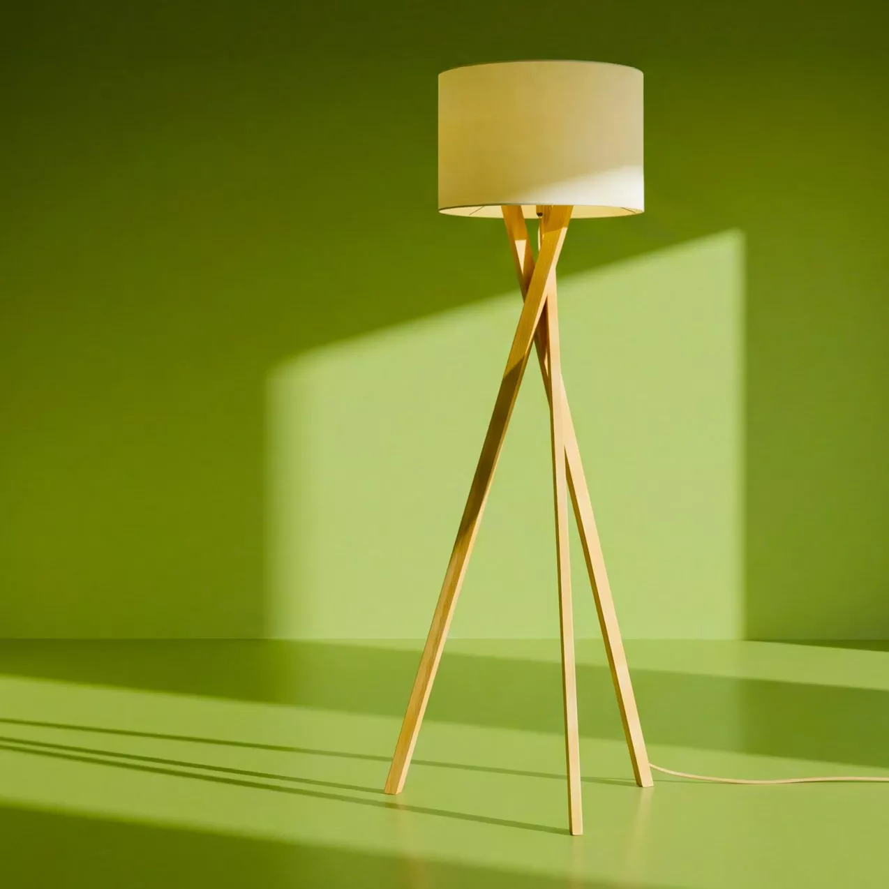 Minimalist wooden tripod floor lamp with cream shade against a green wall, modern Scandinavian interior lighting