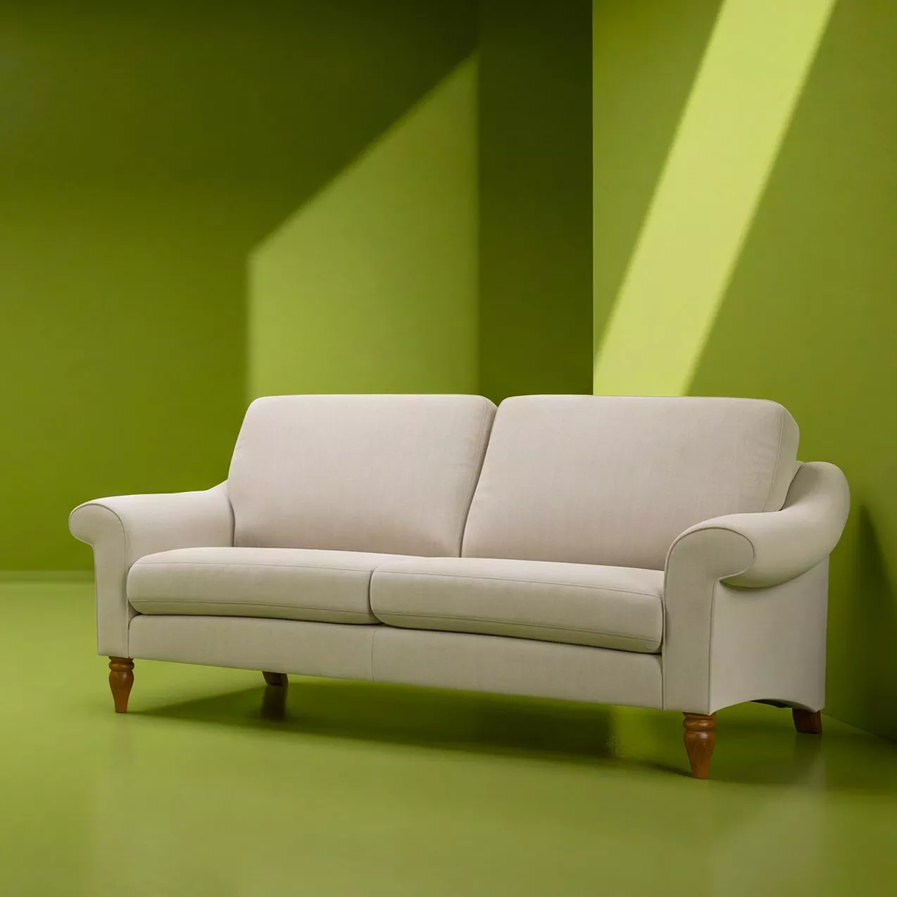 Cream upholstered two-seater sofa with wooden legs in a modern green room with sunlight and shadows