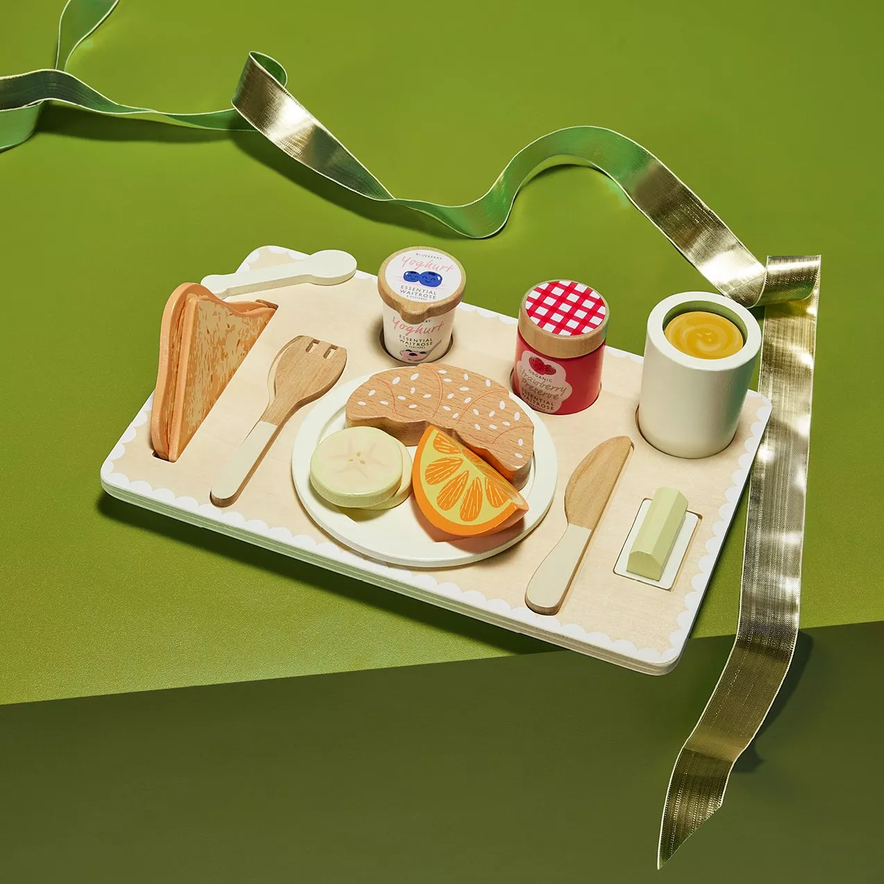 Wooden toy breakfast tray with bread, yoghurt, jam, orange slices and egg cup on green background