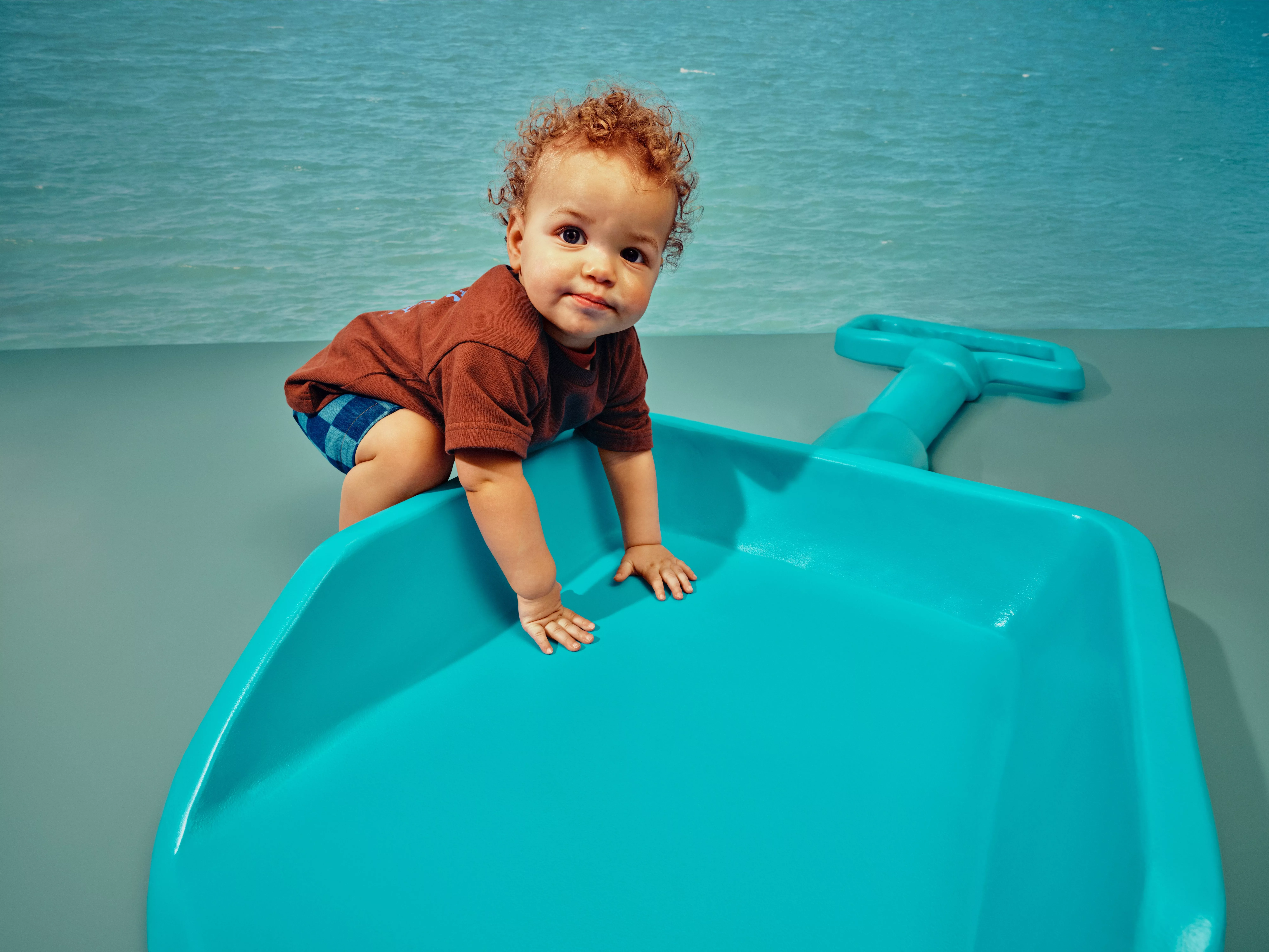Toddler climbing a turquoise plastic playground slide by the sea, outdoor family holiday fun in summer